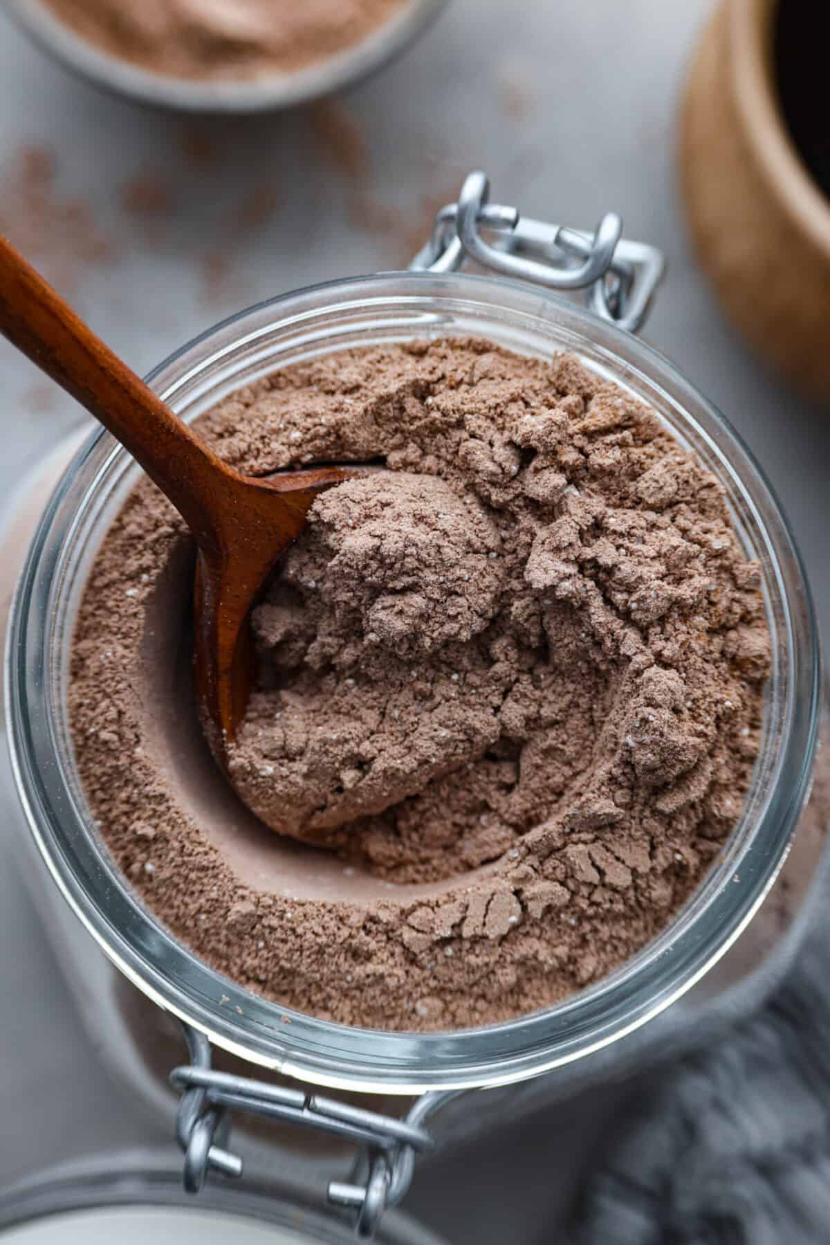 Delicious homemade hot chocolate mix that you can enjoy all winter long! It’s easy to customize and makes a perfectly rich and creamy cup of hot cocoa every time. Top-down view of hot chocolate mix in a glass jar, being mixed with a wooden spoon.