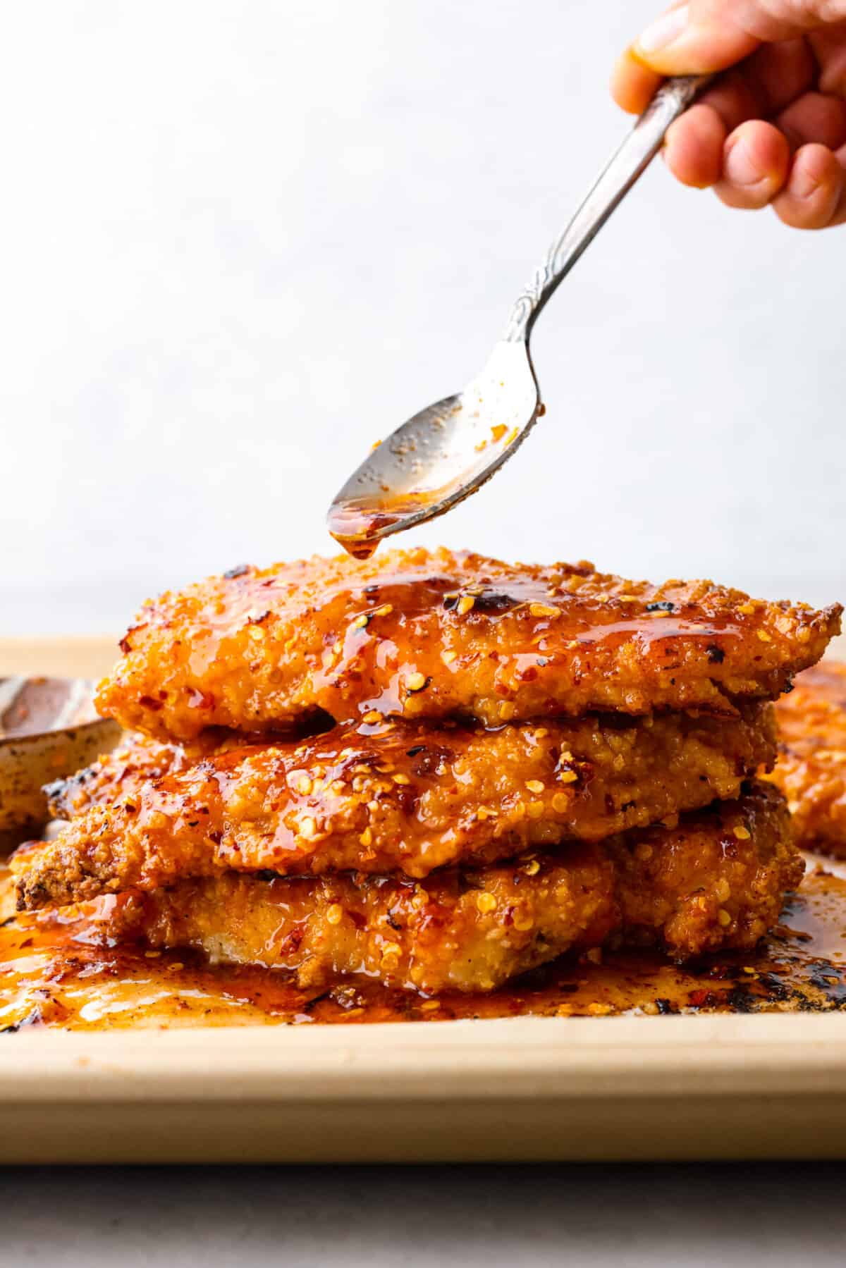 Your new favorite chicken recipe. This hot honey chicken is perfectly crispy and coated in a honey glaze that packs a punch! Honey, hot sauce, chili flakes, and garlic make the flavor so addictive, you won't be able to get enough. 3 pieces of chicken stacked on top of each other, coated in a spicy glaze.