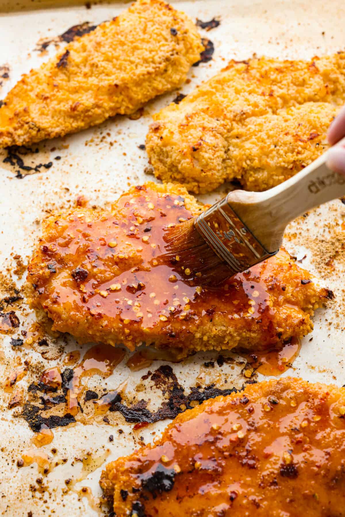 Your new favorite chicken recipe. This hot honey chicken is perfectly crispy and coated in a honey glaze that packs a punch! Honey, hot sauce, chili flakes, and garlic make the flavor so addictive, you won't be able to get enough. Brushing sauce over a piece of hot honey chicken.