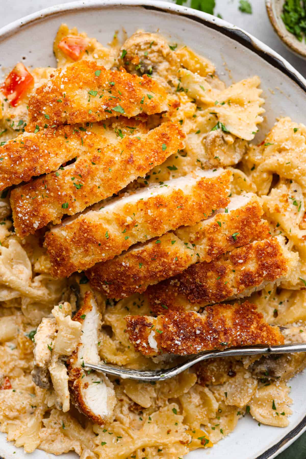 Breaded, crispy chicken cutlets and a creamy Cajun sauce come together in this AMAZING Louisiana chicken pasta recipe. Inspired by Cheesecake Factory, you're going to love making this at home! Closeup of sliced, breaded chicken.