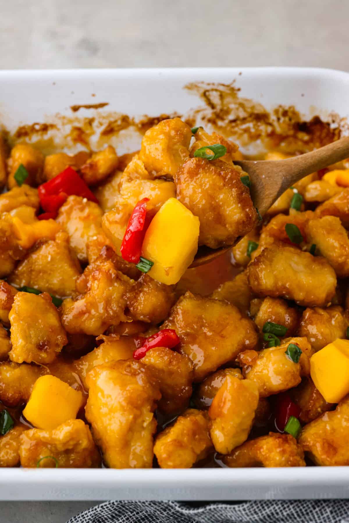 Bright and vibrant Mango Chicken is a flavorful, unique dinner that the whole family will enjoy! Tender chicken pieces are browned, and then baked in a sweet and tangy mango sauce. Serve with rice to soak up all of the delicious sauce! Closeup of chicken topped with mango and chopped red bell peppers.