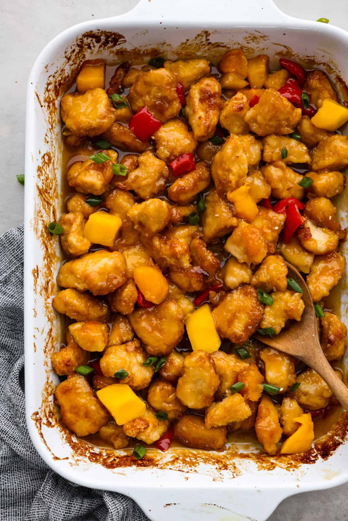 Bright and vibrant Mango Chicken is a flavorful, unique dinner that the whole family will enjoy! Tender chicken pieces are browned, and then baked in a sweet and tangy mango sauce. Serve with rice to soak up all of the delicious sauce! Top-down view of mango chicken in a white baking dish.