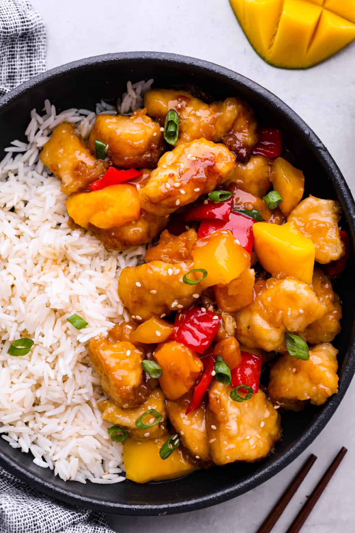 Bright and vibrant Mango Chicken is a flavorful, unique dinner that the whole family will enjoy! Tender chicken pieces are browned, and then baked in a sweet and tangy mango sauce. Serve with rice to soak up all of the delicious sauce! Mango chicken served with white rice in a black bowl.