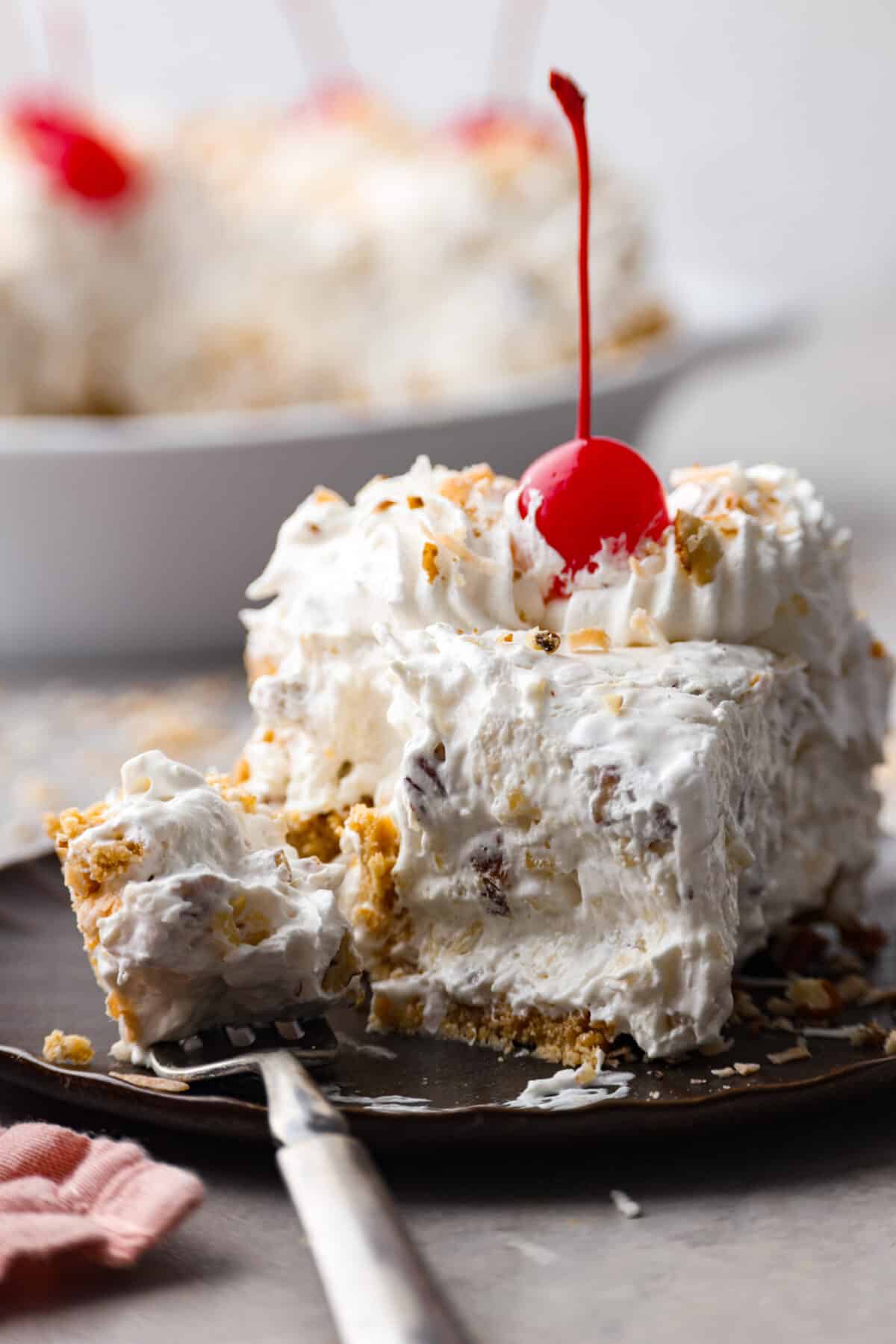 Named 'Million Dollar Pie' because it's so rich and delicious, this scrumptious dessert is the perfect way to satisfy your sweet tooth! It's light and fluffy but packed with coconut, pecans, and pineapple for tasty tidbits in each bite! Closeup of a slice of pie with a bite taken out of it.
