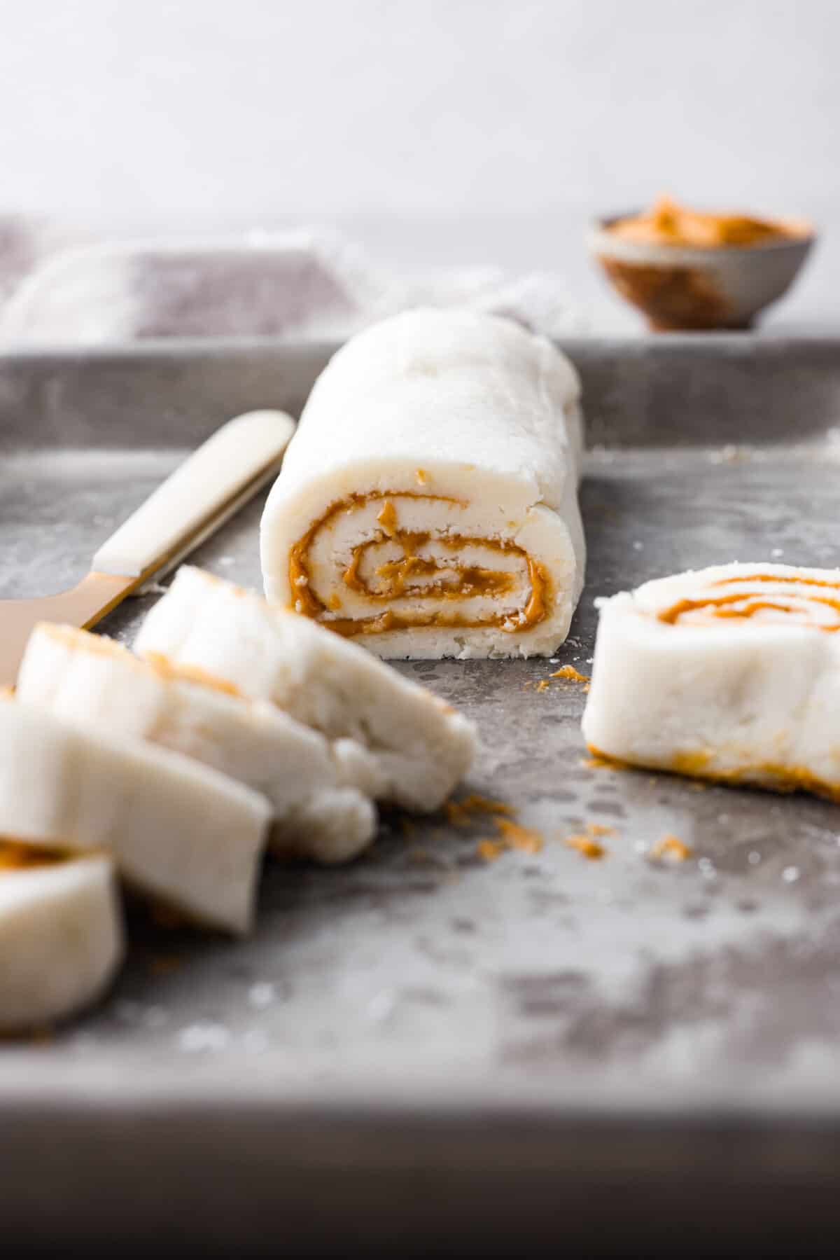 This Peanut Butter Pinwheel Candy recipe has been passed down in my family for generations! These are soft, fluffy, and full of amazing peanut butter flavor. You won't believe what the secret ingredient is that makes these so incredible! Side shot of a peanut butter pinwheel candy roll with slices in the foreground.