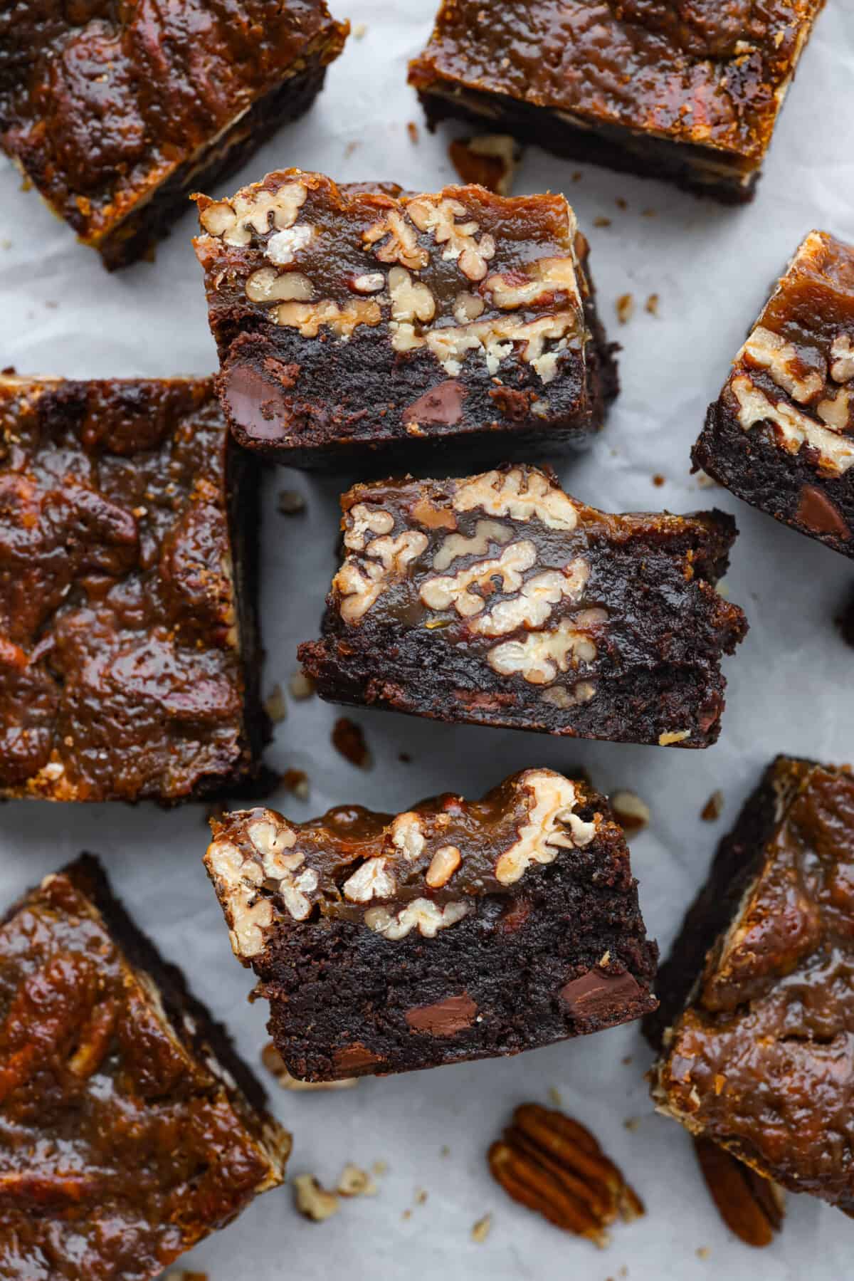 Two amazing desserts come together with these delicious pecan pie brownies! Theyโre rich and fudgy with a gooey pecan pie topping that will have you reaching for another piece. Overhead shot of pecan pie brownies cut into squares, some on their sides.