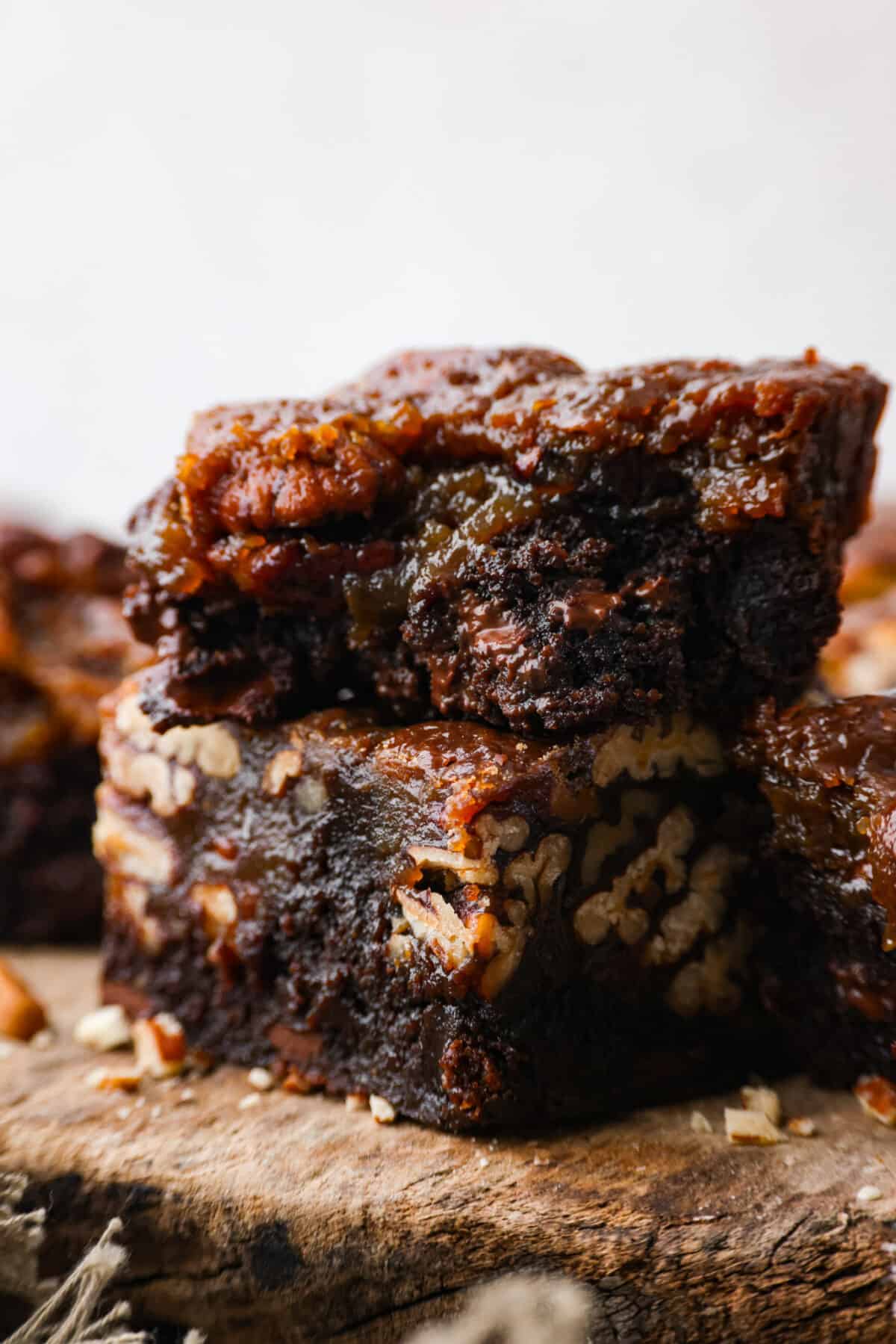 Two amazing desserts come together with these delicious pecan pie brownies! Theyโre rich and fudgy with a gooey pecan pie topping that will have you reaching for another piece. Close up shot of pecan pie brownies stacked on each other.
