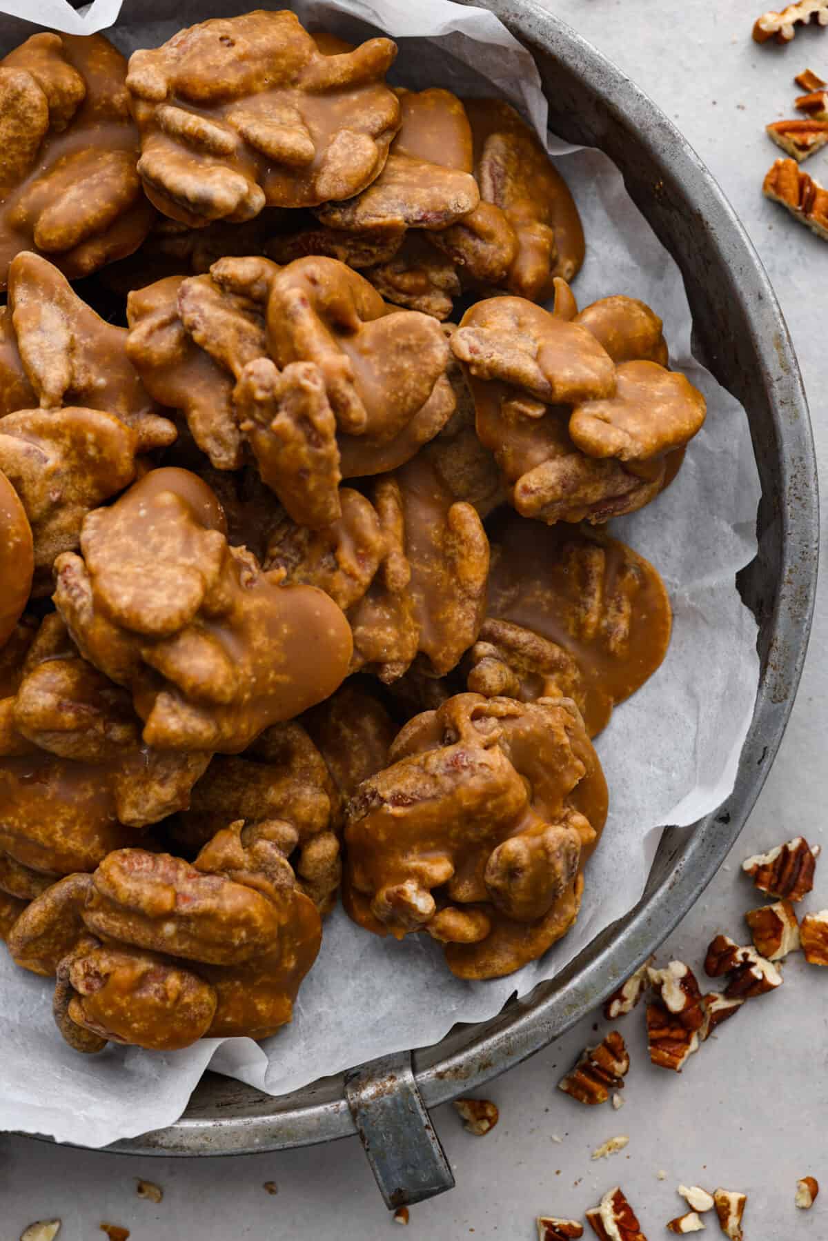 If you have a sweet tooth, this Pecan Praline recipe is for you! An ooey gooey combination of sweet flavors and a crunchy texture, this recipe is perfect for any occasion. The top view of pralines in a tin pan with some parchment paper.