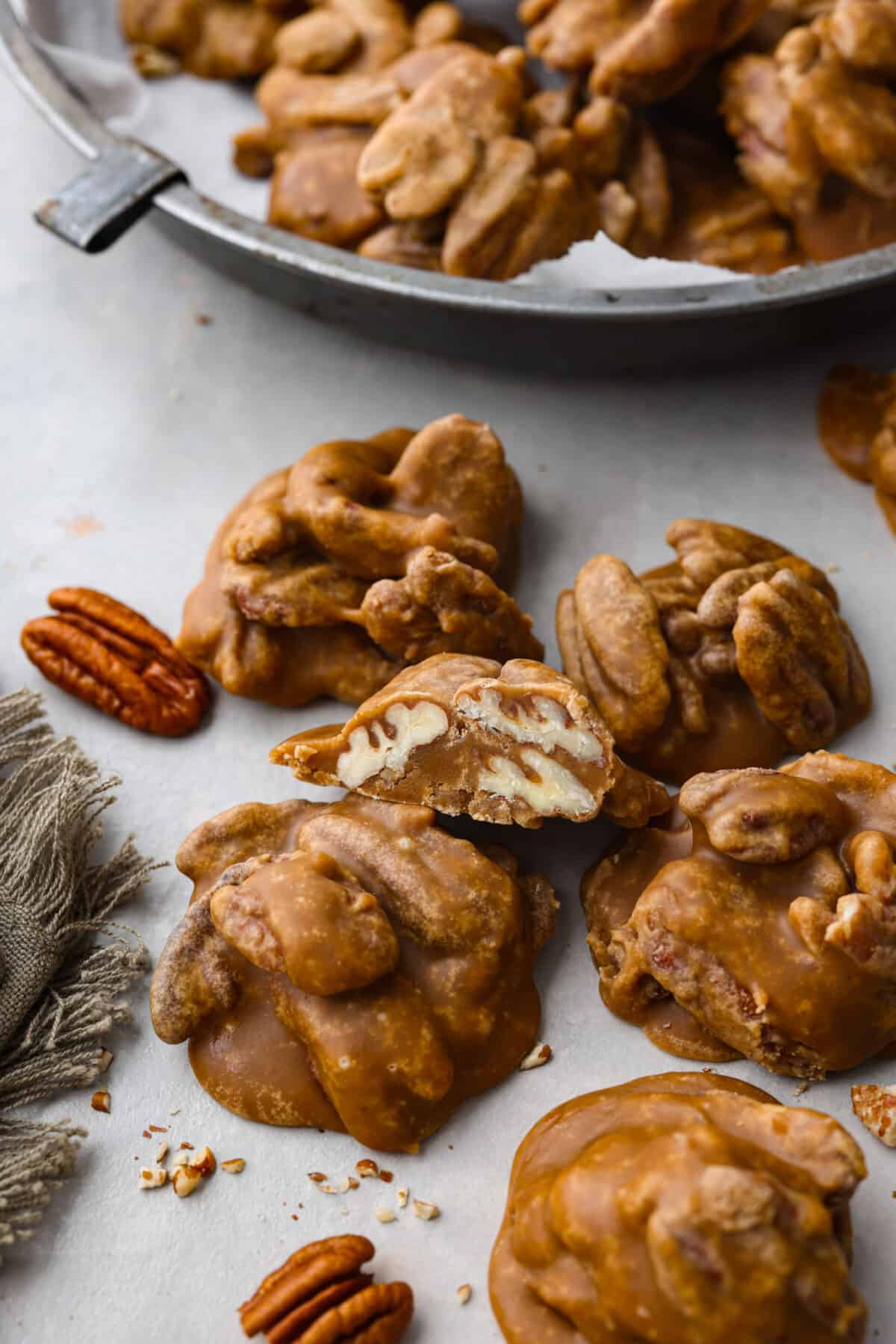 If you have a sweet tooth, this Pecan Praline recipe is for you! An ooey gooey combination of sweet flavors and a crunchy texture, this recipe is perfect for any occasion. Pecan pralines on parchment paper. One cut in half so that you can see the pecans inside.