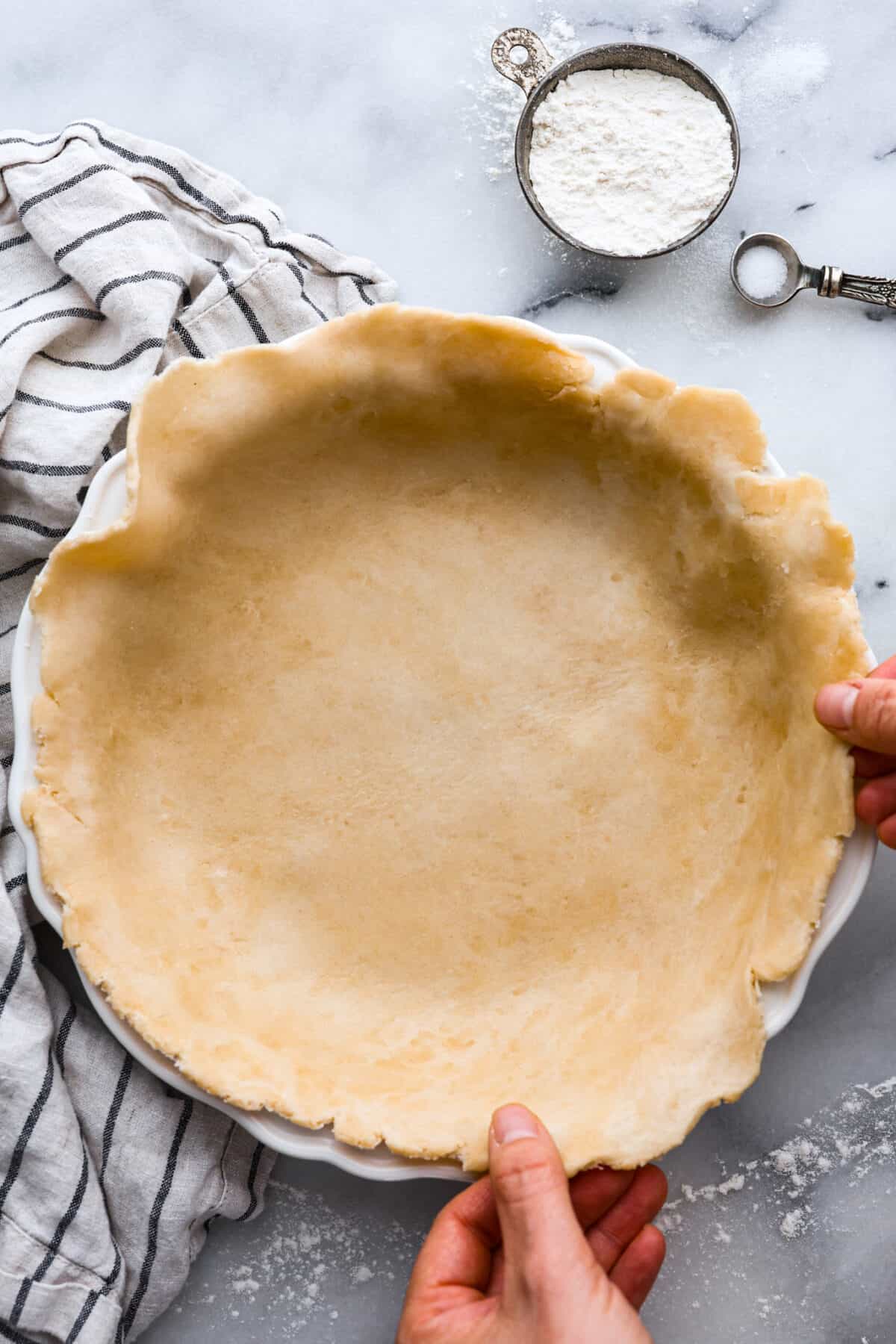 Tender, buttery, and easy-to-make, my Grandma's perfect pie crust is everything you need this Thanksgiving. It's so foolproof, you won't use store-bought ever again! A pie crust being put into a pan.