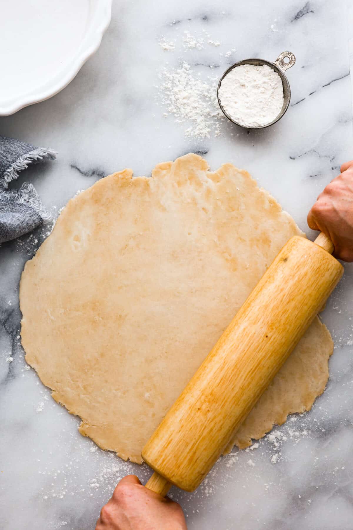 Tender, buttery, and easy-to-make, my Grandma's perfect pie crust is everything you need this Thanksgiving. It's so foolproof, you won't use store-bought ever again! Pie dough being rolled out with a wooden roller.