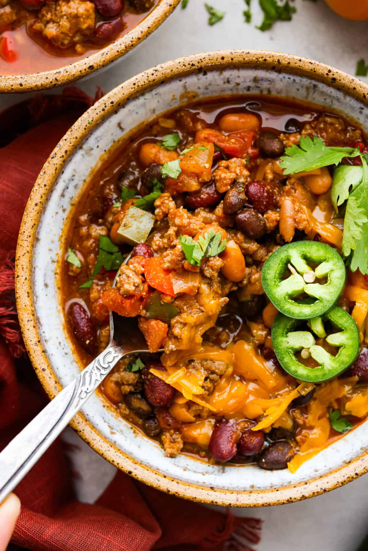 Pumpkin chili is the perfect hearty meal for cold weather. It features perfectly seasoned ground beef, tender beans, and velvety pumpkin puree. Each bowl is packed with fall flavor, making it a cozy and delicious choice for chilly days. Closeup of the pumpkin chilli, topped with cheese and jalapenos.