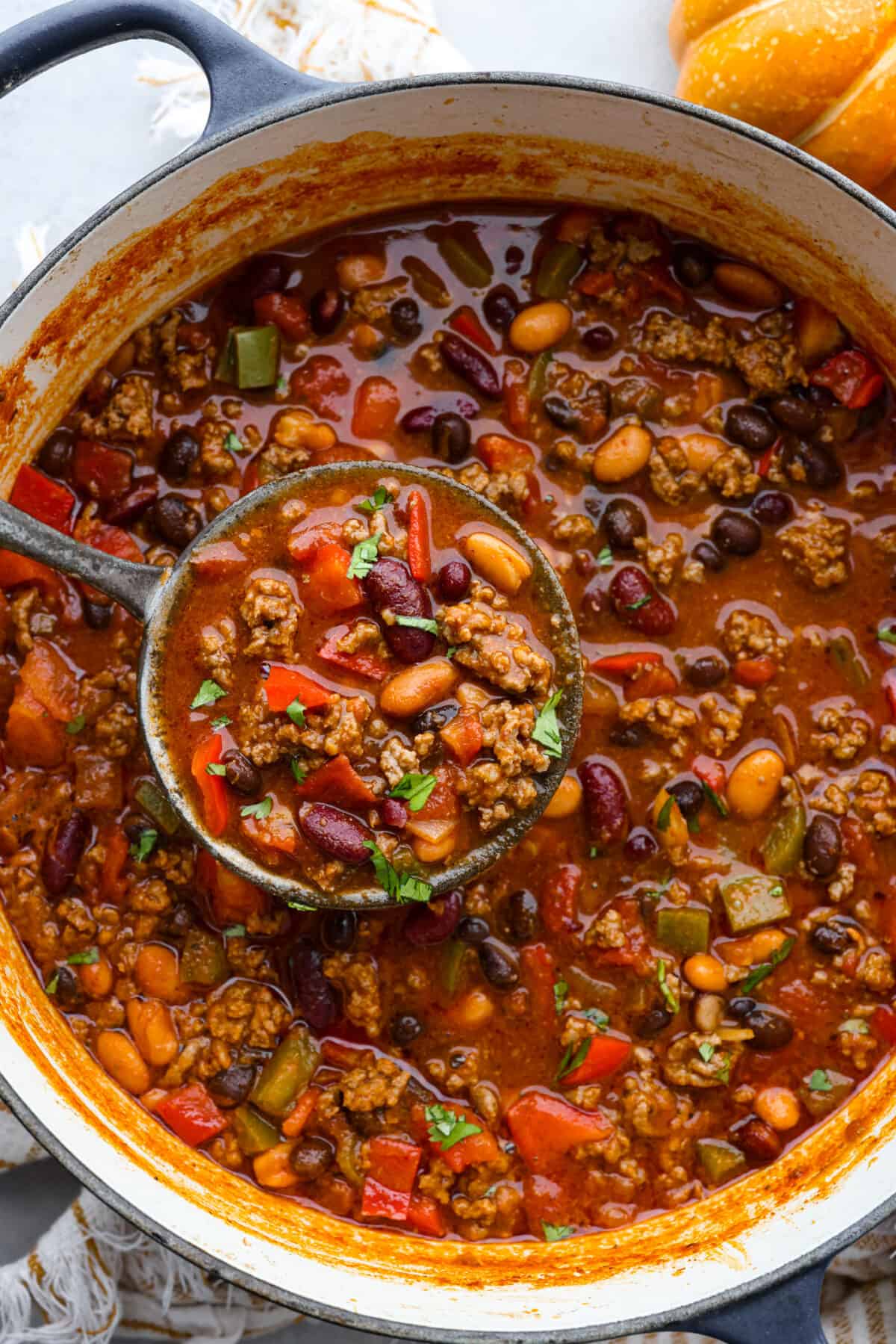 Pumpkin chili is the perfect hearty meal for cold weather. It features perfectly seasoned ground beef, tender beans, and velvety pumpkin puree. Each bowl is packed with fall flavor, making it a cozy and delicious choice for chilly days. Pumpkin chili in a large blue and white pot, being scooped up with a ladle.