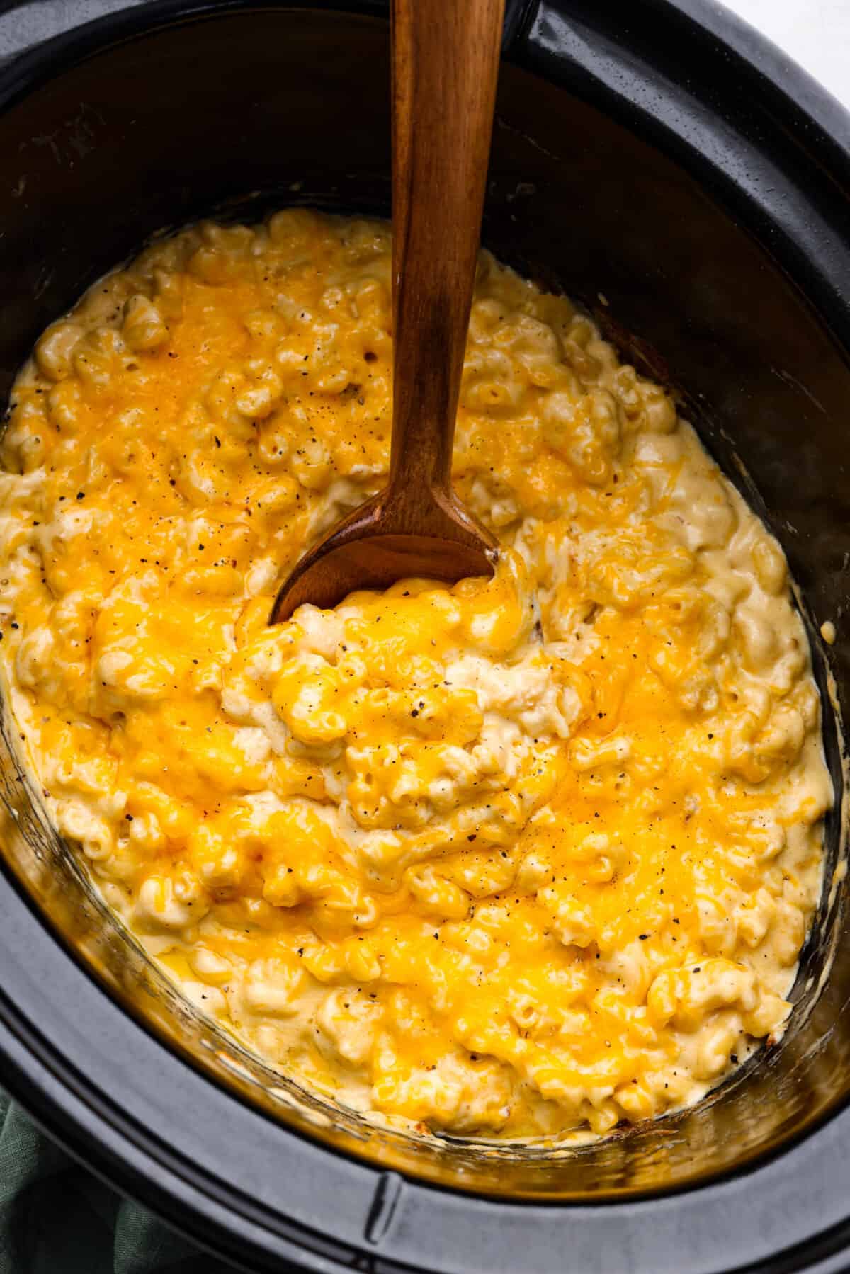 This Slow Cooker Macaroni and Cheese is creamy, comforting and perfect for potlucks. Best of all, it comes together easily in the crock-pot โ even the pasta! Macaroni and cheese in the bottom of a slow cooker, being mixed with a wooden spoon.