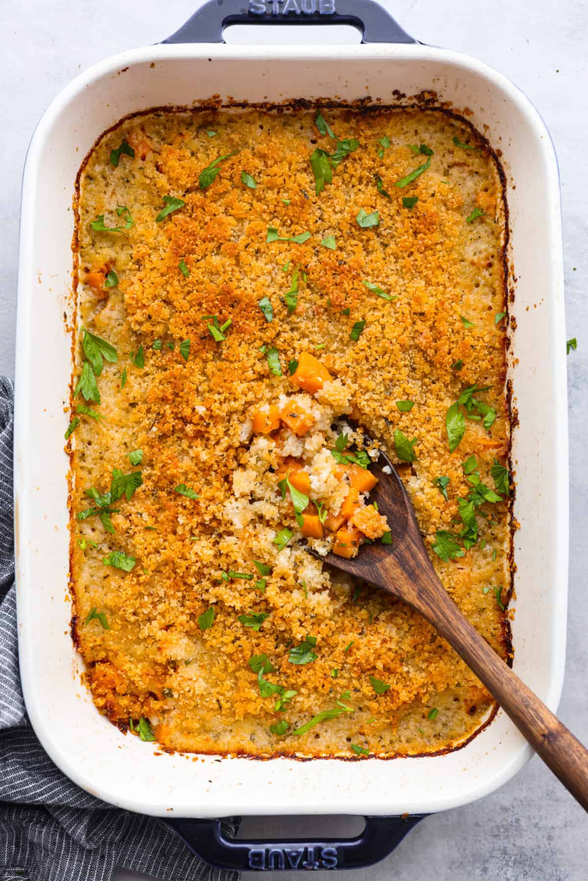 Savory Sweet Potato Casserole is a delicious new way to enjoy this classic Thanksgiving side dish! Tender bite-sized pieces of sweet potato are combined with fresh herbs and seasonings, sprinkled with a cheesy crispy topping, and baked to perfection. This recipe is easy enough for weeknight dinners, yet it's perfect for the holidays, too! Top-down view of savory sweet potato casserole in a white baking dish.