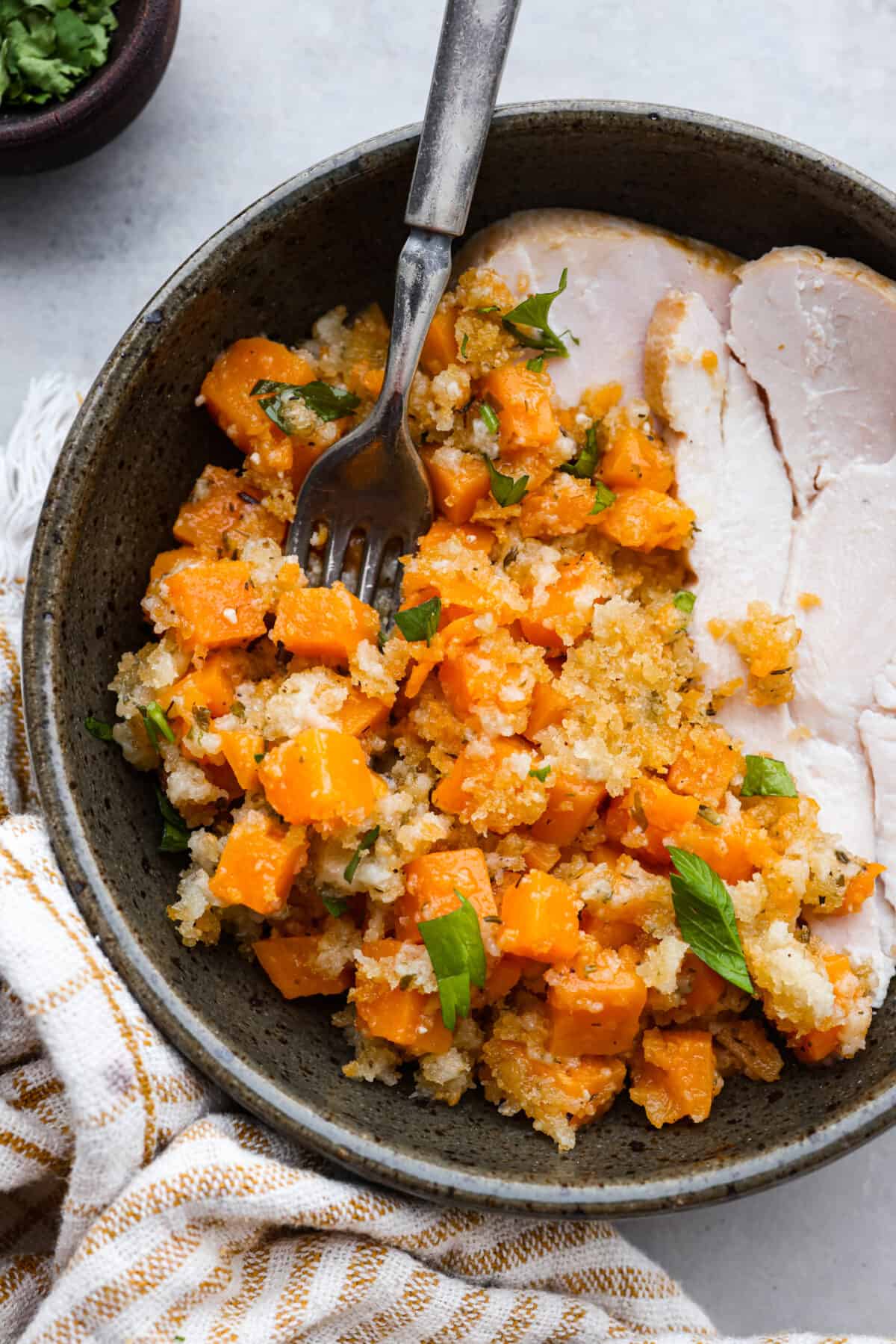 Savory Sweet Potato Casserole is a delicious new way to enjoy this classic Thanksgiving side dish! Tender bite-sized pieces of sweet potato are combined with fresh herbs and seasonings, sprinkled with a cheesy crispy topping, and baked to perfection. This recipe is easy enough for weeknight dinners, yet it's perfect for the holidays, too! Turkey and sweet potato casserole served in a gray bowl.