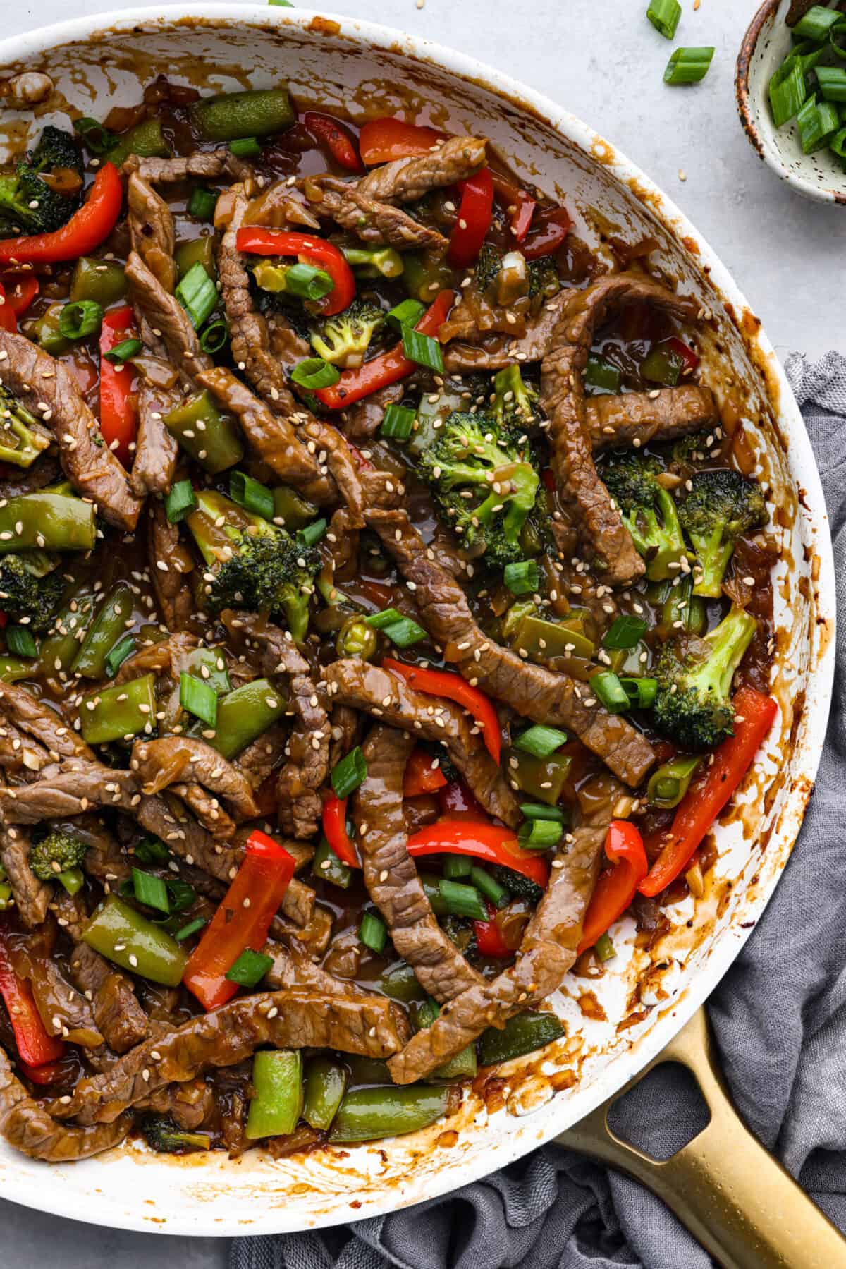 Delicious Szechuan Beef is filled with mouthwatering bold flavor! Tender strips of beef, bell peppers, snap peas, and broccoli are stir-fried together with a perfectly sweet, spicy, tangy sauce. It's way better than takeout and cooks up in under 20 minutes! Top-down view of cooked szechuan beef in a skillet.