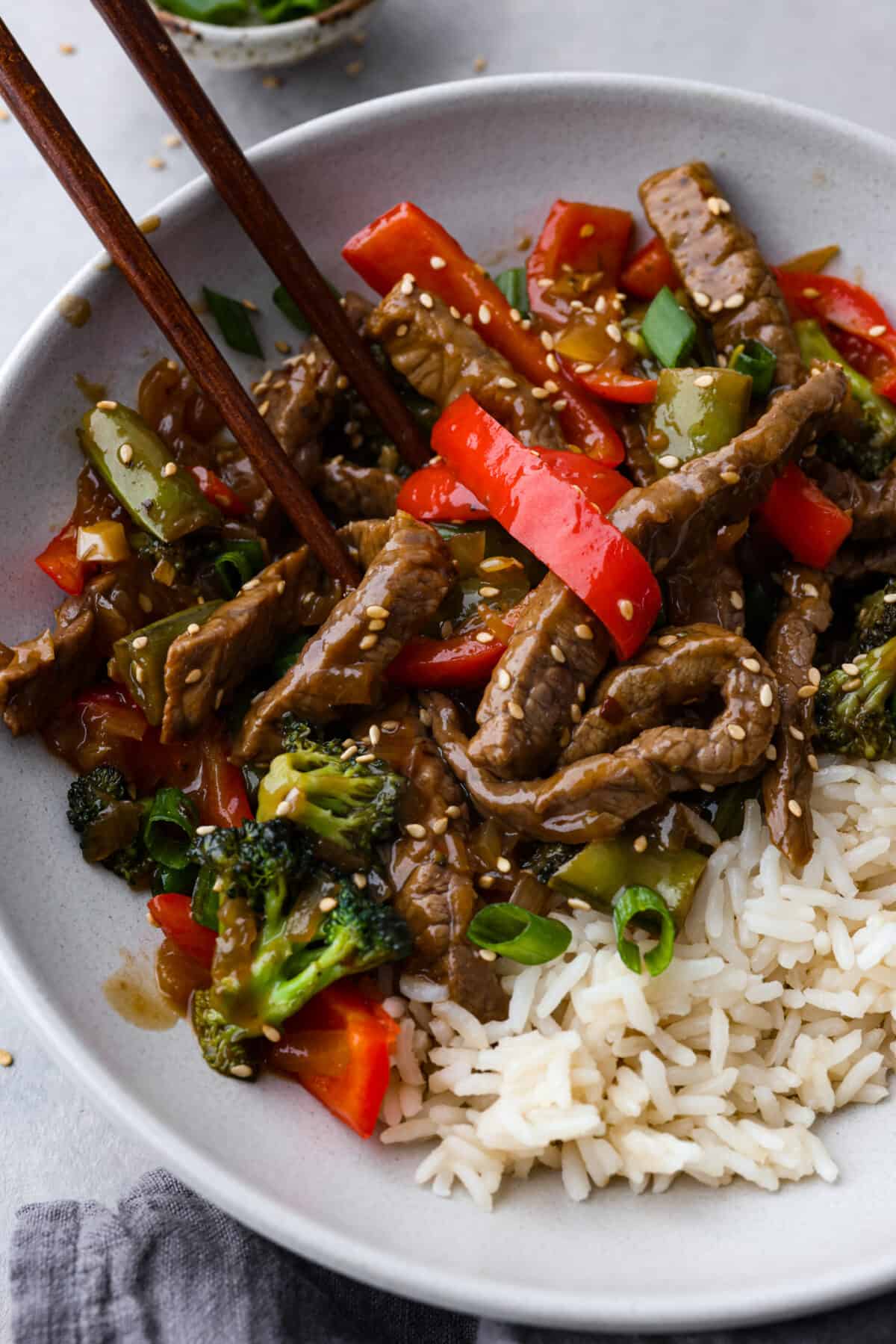 Delicious Szechuan Beef is filled with mouthwatering bold flavor! Tender strips of beef, bell peppers, snap peas and broccoli are stir-fried together with a perfectly sweet, spicy, tangy sauce. It's way better than takeout and cooks up in under 20 minutes! A bowl of szechuan beef served with chopsticks.