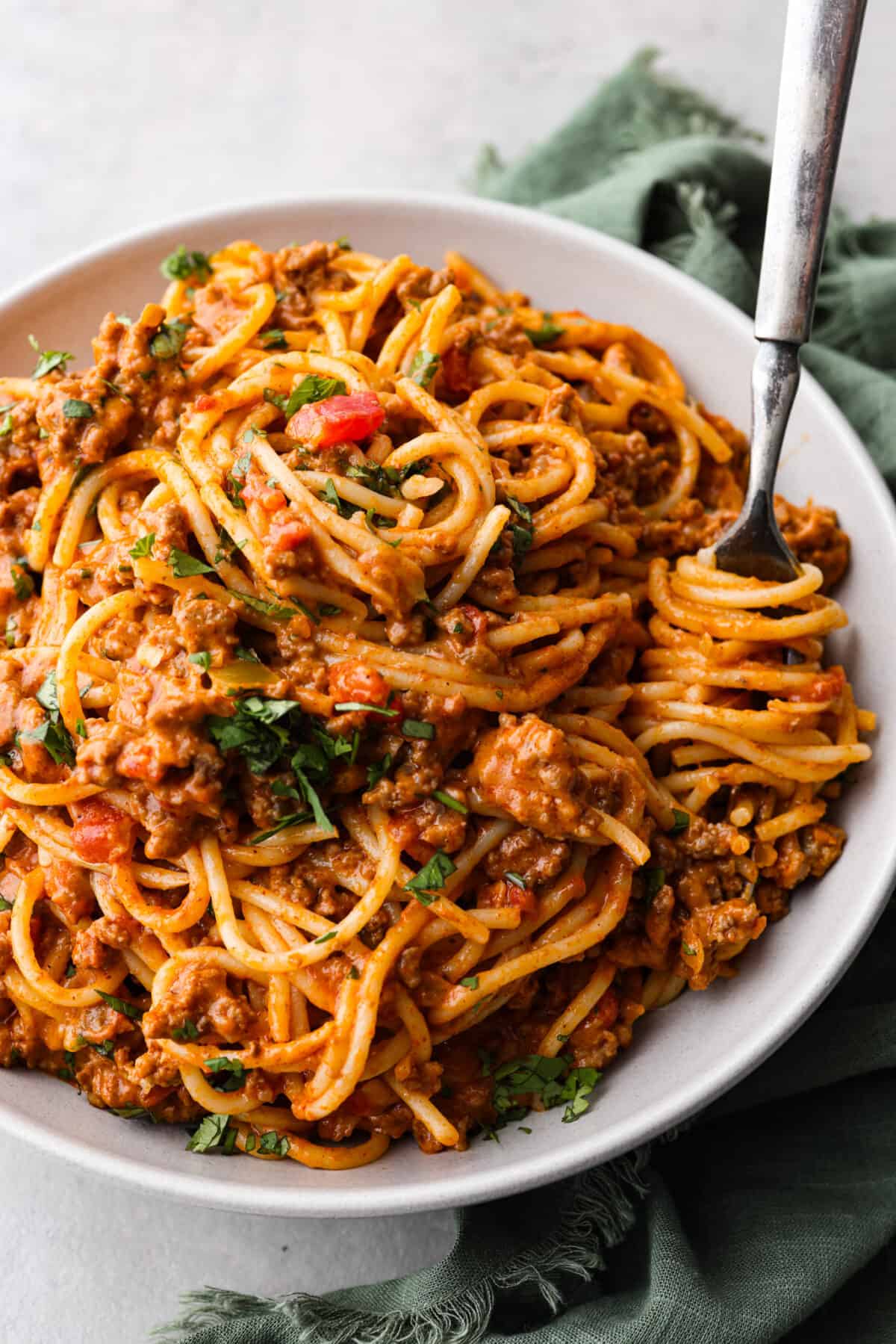 Taco spaghetti brings together two family favorites, tacos and pasta, in one cheesy, flavor packed dish! With taco-seasoned beef, melty cheese, and zesty tomatoes, itโs a weeknight win everyone will love. A serving of taco spaghetti, topped with fresh herbs.