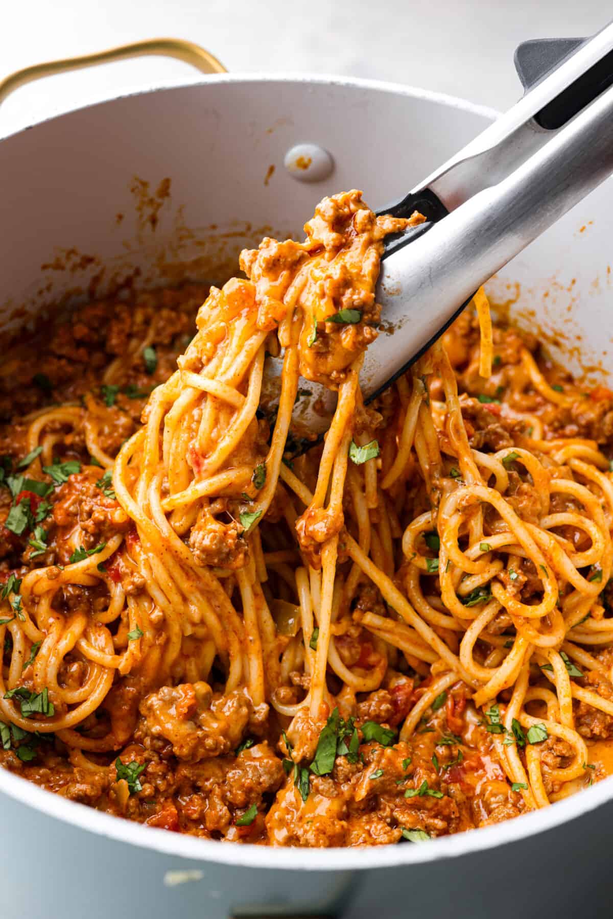 Taco spaghetti brings together two family favorites, tacos and pasta, in one cheesy, flavor packed dish! With taco-seasoned beef, melty cheese, and zesty tomatoes, itโs a weeknight win everyone will love. Taco spaghetti in a large pot, being picked up with tongs.