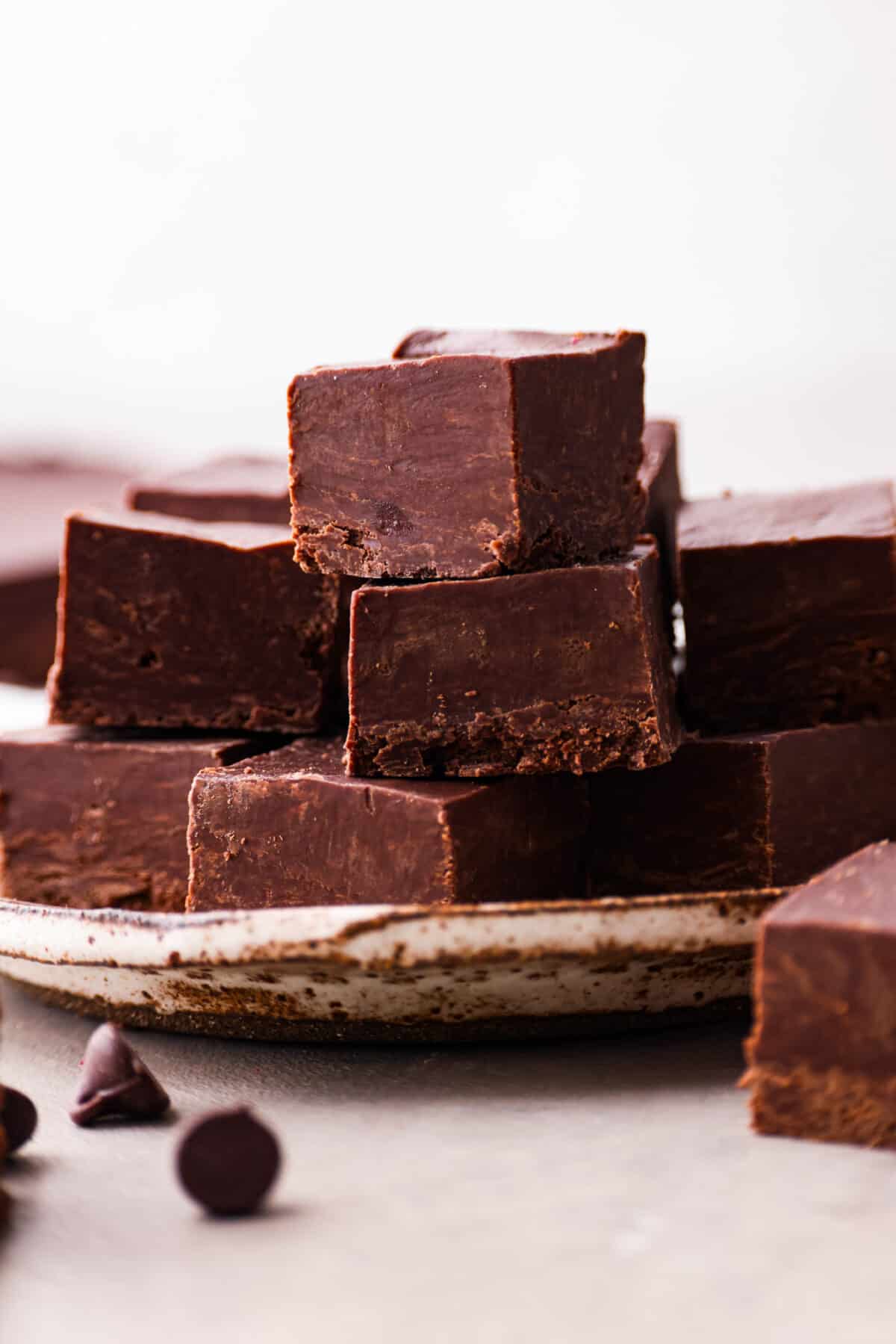 It doesn't get any easier than this homemade 2 ingredient fudge! Creamy and decadent fudge that only takes 5 minutes to make. Perfect for parties and gifting! Close view of 2 ingredient fudge pieces stacked on a plate.