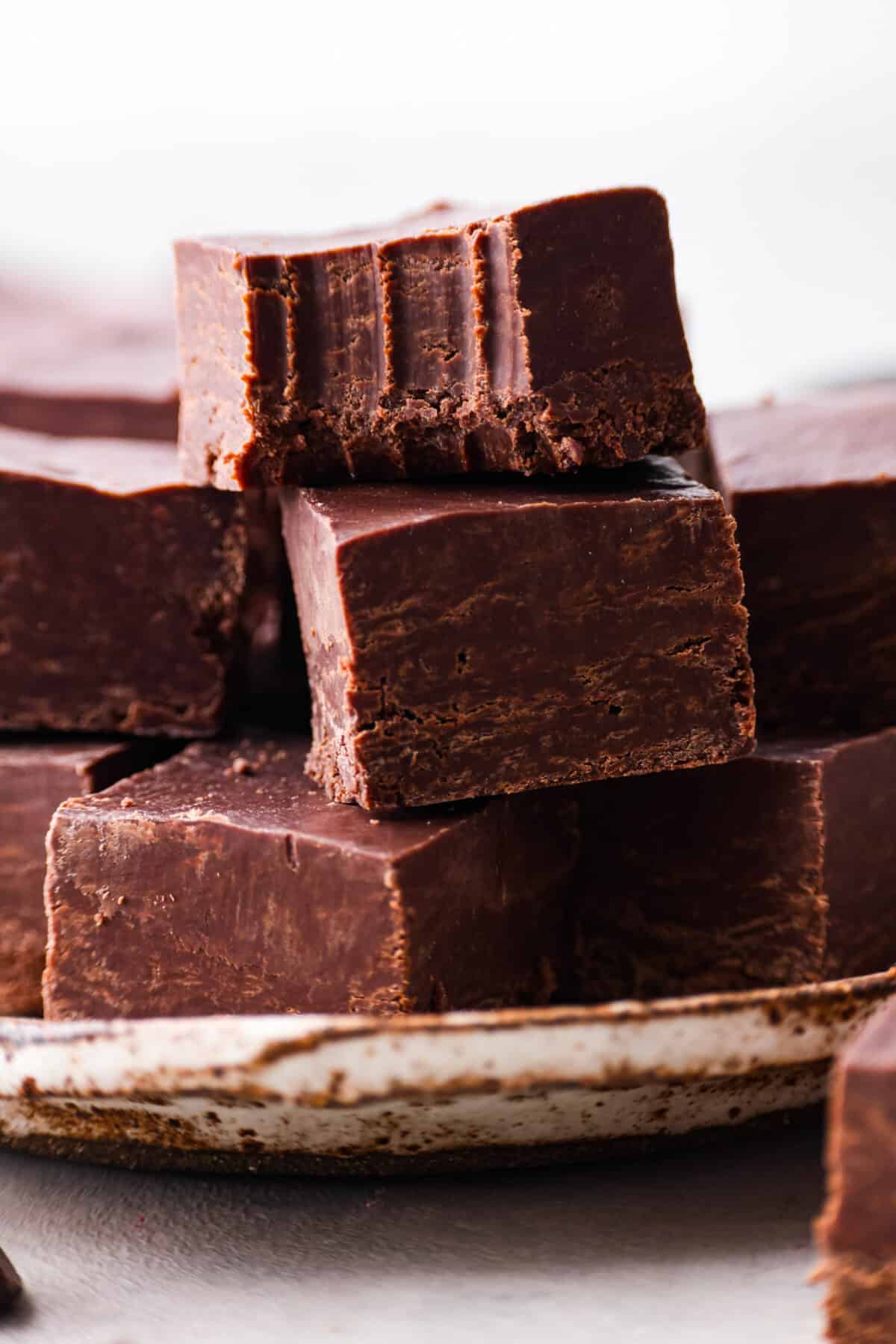 It doesn't get any easier than this homemade 2 ingredient fudge! Creamy and decadent fudge that only takes 5 minutes to make. Perfect for parties and gifting! Close view of 2 ingredient fudge squares stacked on a plate. The top piece of fudge has a bite out of it.