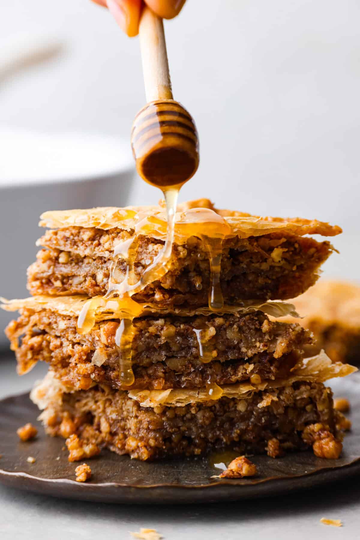 Phyllo pastry and walnuts are layered together then baked until the pastry is deliciously flaky. A sweet honey syrup is poured over the top which soaks into the baklava and makes every bite heavenly. 3 pieces of baklava, being coated in honey syrup.