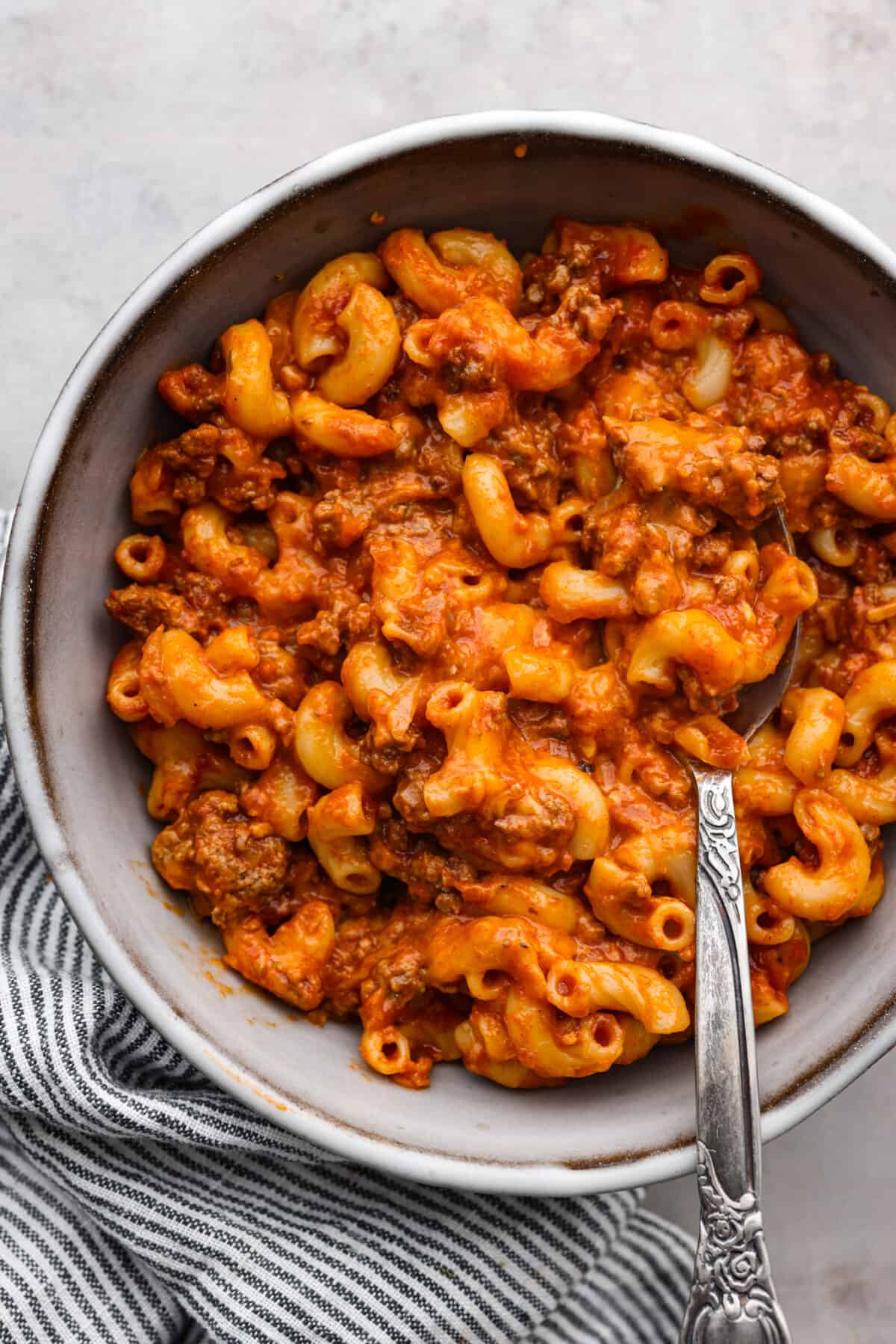 Craving cheesy, saucy comfort food that's perfect for a weeknight meal? This hearty beefaroni is the way to go. Each macaroni noodle traps the cheesy, meaty, garlicky sauce inside, so every bite has incredible flavor. Easy to prepare and picky eater-approved, this is one dinner you don't want to miss out on. Top-down view of a serving of beefaroni in a gray bowl.