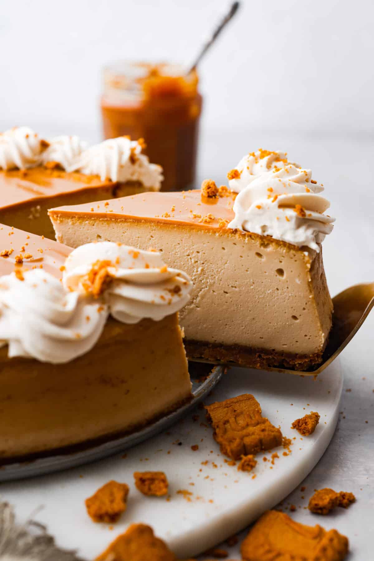 Soft, rich, and loaded with delicious cookie butter flavor, this Biscoff cheesecake is sure to please! Everyone will be lining up for a slice. Closeup of a slice of Biscoff cheesecake on a metal cake spatula.