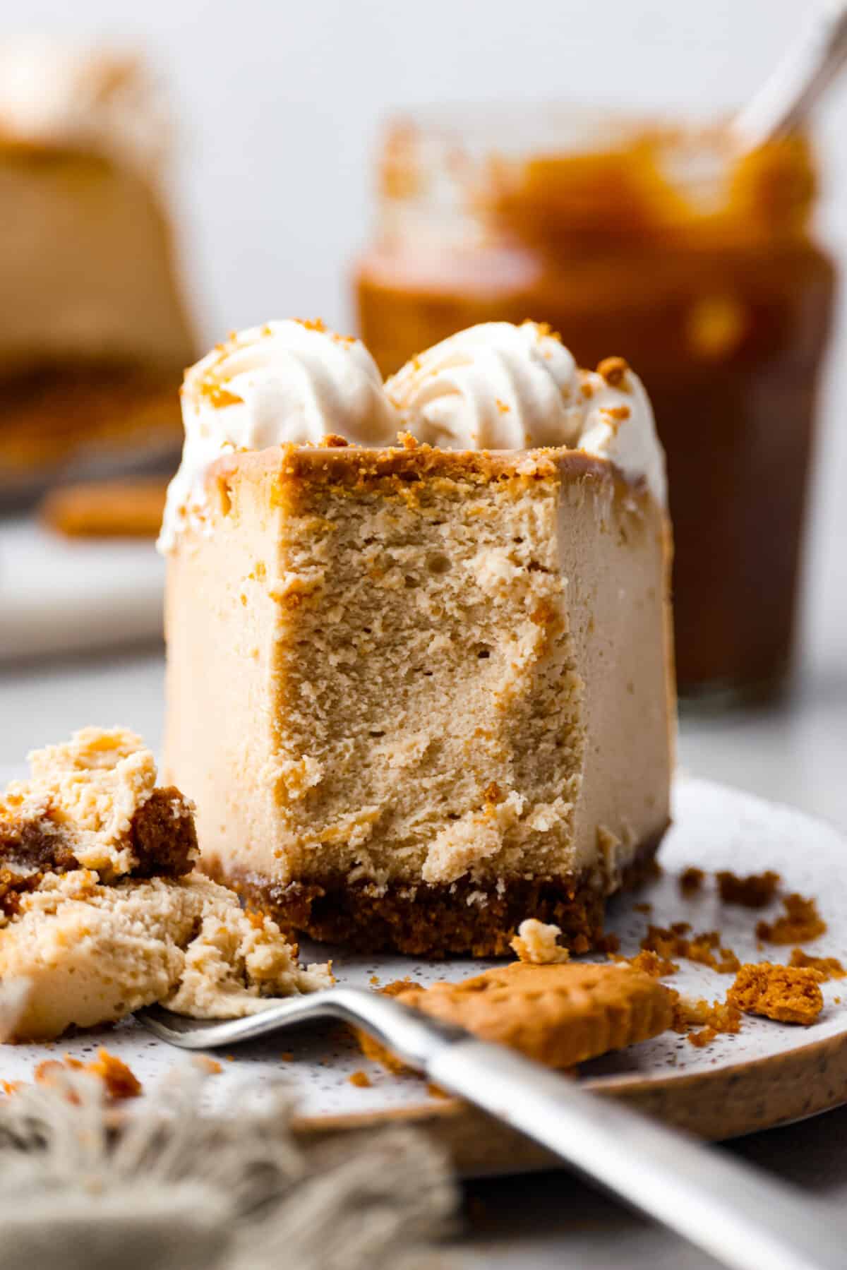 Soft, rich, and loaded with delicious cookie butter flavor, this Biscoff cheesecake is sure to please! Everyone will be lining up for a slice. Front view of a slice of cheesecake with a bite taken out of it.