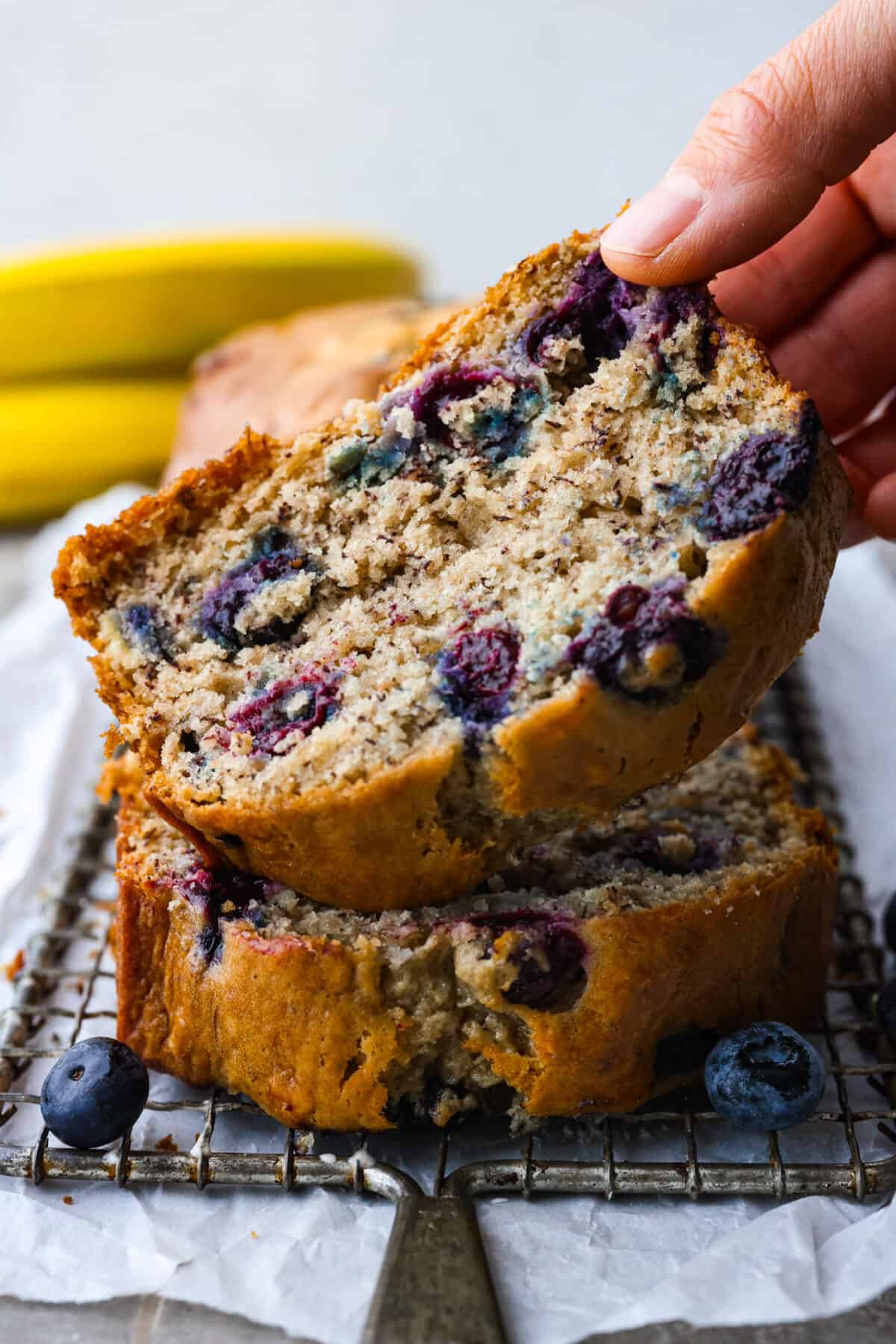 This moist and delicious blueberry banana bread is something anyone can make, and that everyone will love. Packed with juicy berries, each bite of this sweet and tender bread will have you wanting another piece. 2 slices of blueberry banana bread stacked on top of each other.