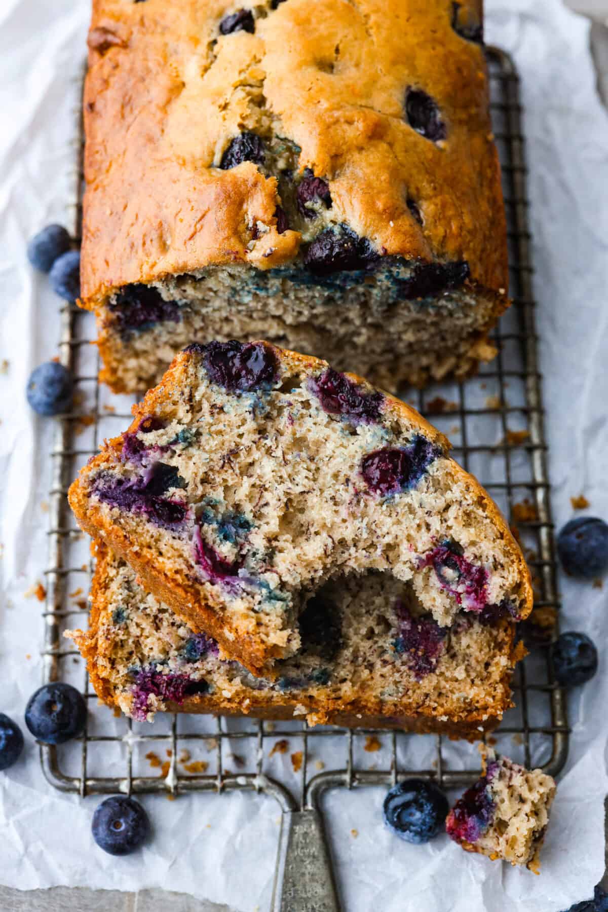 This moist and delicious blueberry banana bread is something anyone can make, and that everyone will love. Packed with juicy berries, each bite of this sweet and tender bread will have you wanting another piece. Banana bread on a cooling rack.