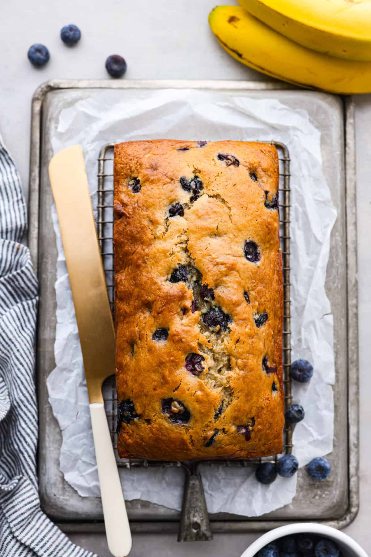 This moist and delicious blueberry banana bread is something anyone can make, and that everyone will love. Packed with juicy berries, each bite of this sweet and tender bread will have you wanting another piece. Top-down view of a loaf of blueberry banana bread.