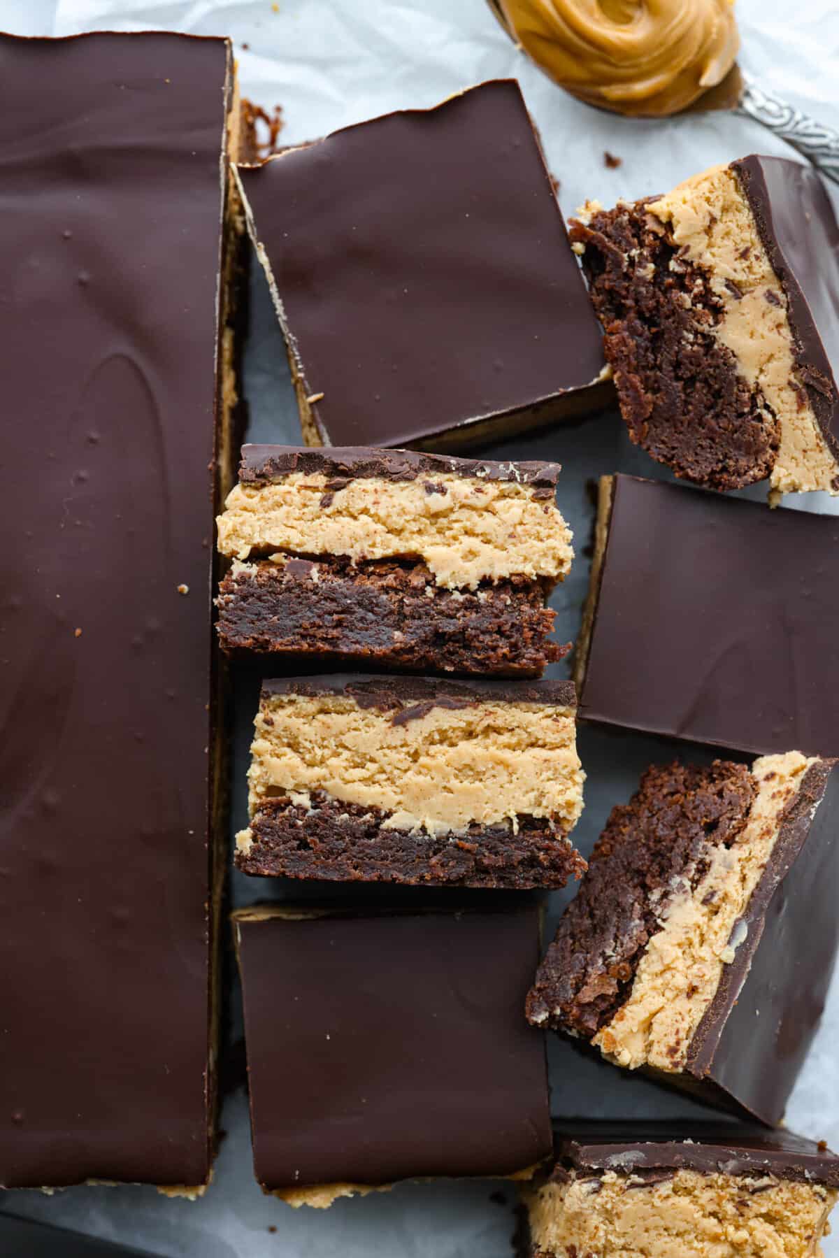 Buckeye brownies are known for their three layers of rich decadent goodness! A fudgy brownie base gets a sweet peanut butter layer then topped with chocolate ganache. It's a chocolate peanut butter lover's dream brownie! Top view of buckeye brownies cut into squares on parchment paper.