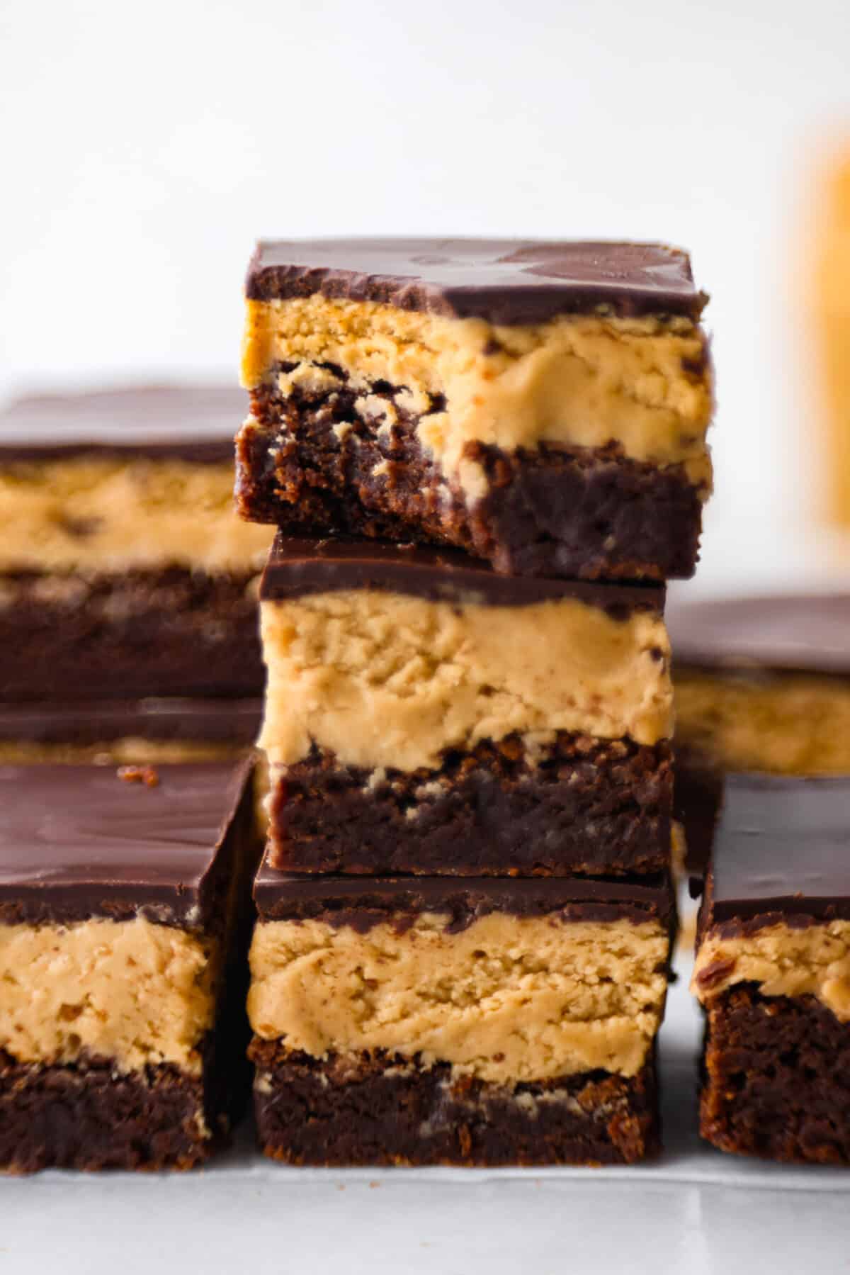 Buckeye brownies are known for their three layers of rich decadent goodness! A fudgy brownie base gets a sweet peanut butter layer then topped with chocolate ganache. It's a chocolate peanut butter lover's dream brownie! Close view of three stacked brownies with a bite out of the top brownie.