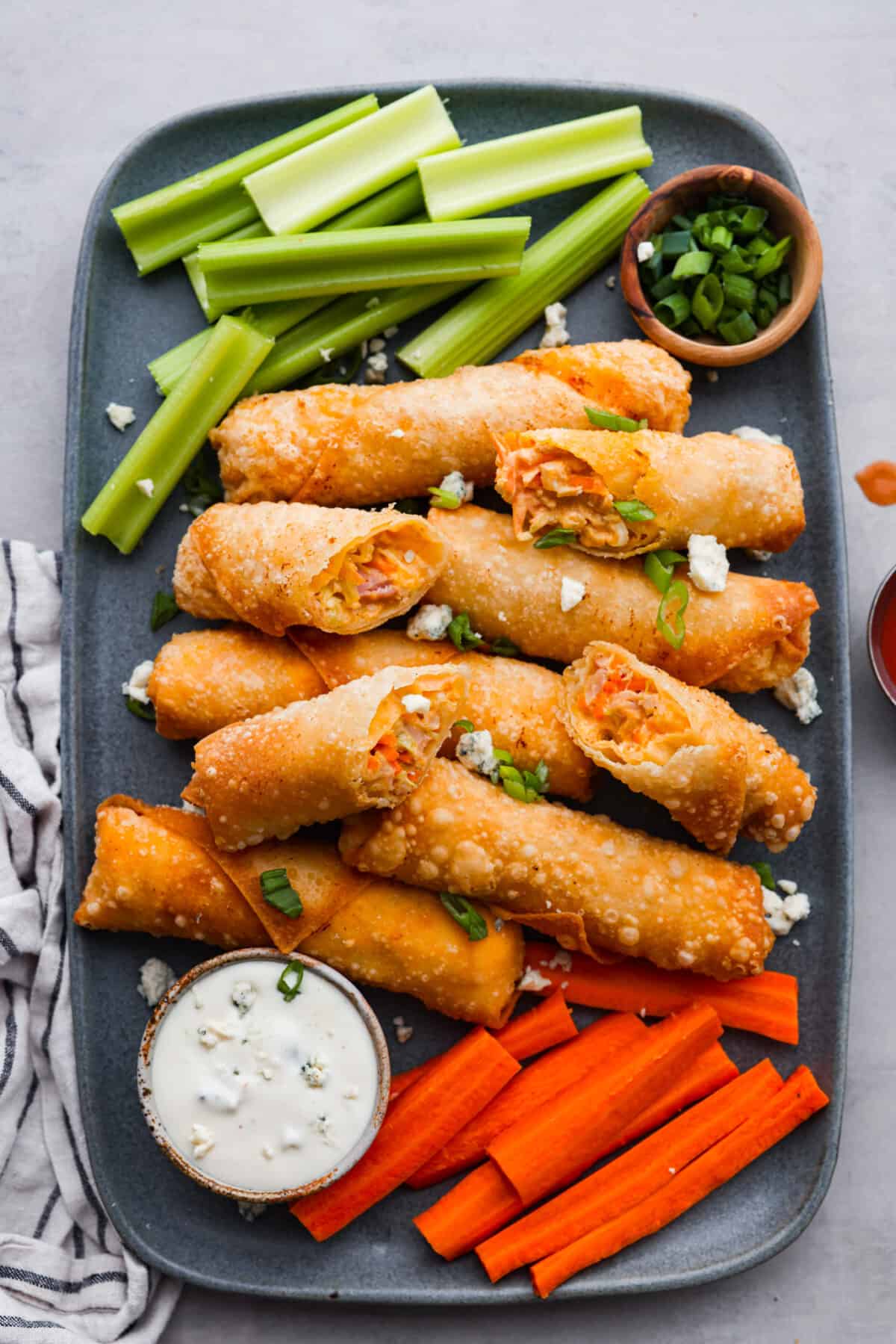 Wait until you taste these Buffalo Chicken Egg Rolls' crispy texture and bold flavors! A delicious mixture of cream cheese, hot sauce, and spices envelops shredded chicken, carrots, and cabbage, creating a perfect balance of crunch and zing. The top view of cooked egg rolls on a platter.