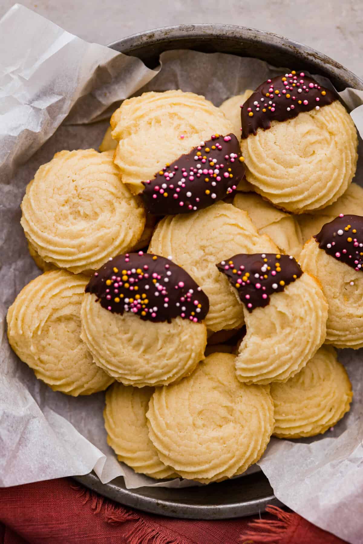 Buttery, tender, and unbelievably light, these homemade Danish butter cookies are so much better than the tinned version. Loaded with flavor, these cookies will melt in your mouth and are so easy to make. Top view of butter cookies in a tin pan lined with parchment paper.