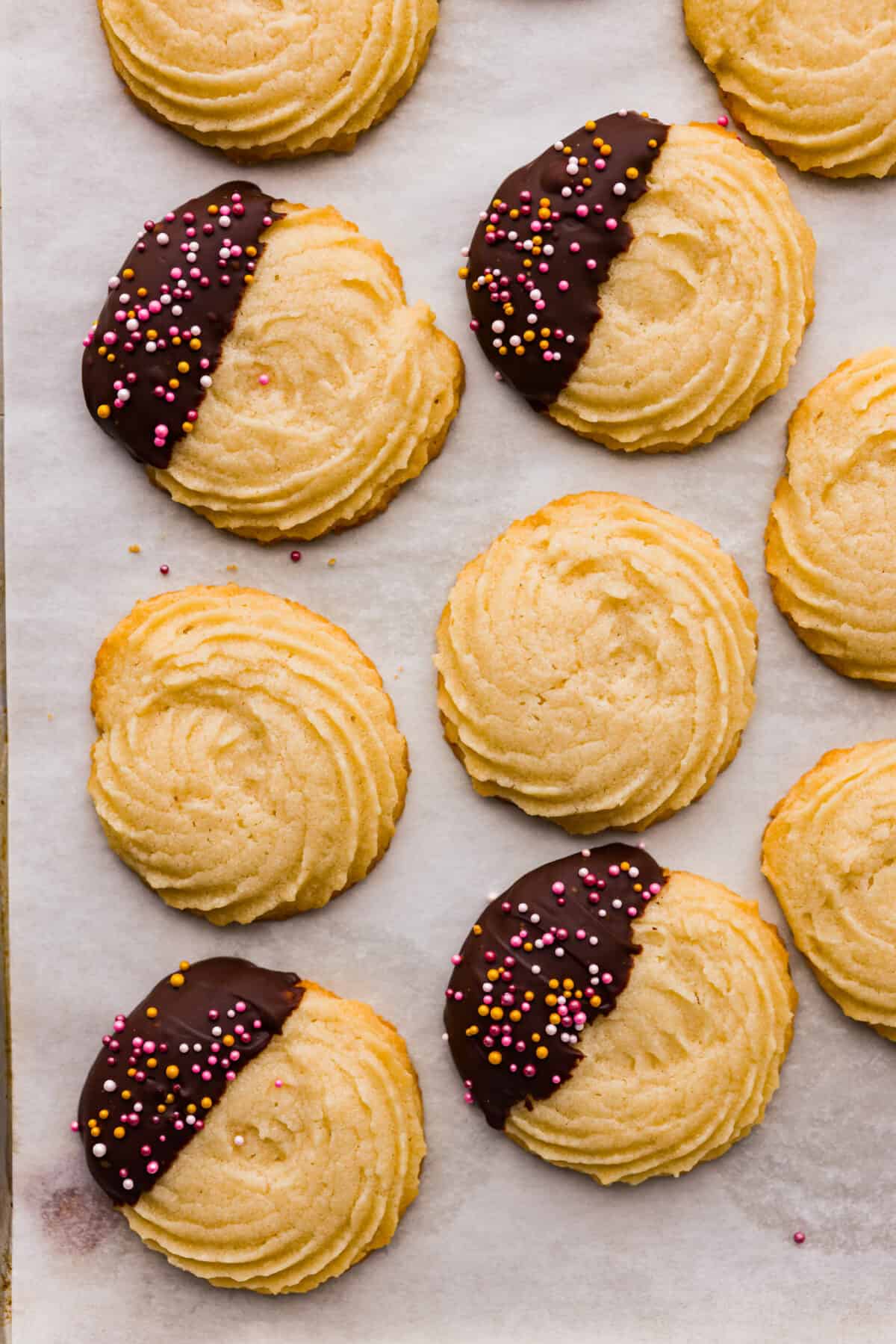 Buttery, tender, and unbelievably light, these homemade Danish butter cookies are so much better than the tinned version. Loaded with flavor, these cookies will melt in your mouth and are so easy to make. Top close view of butter cookies on a baking sheet pan. Some are plain, some are dipped with sprinkles.