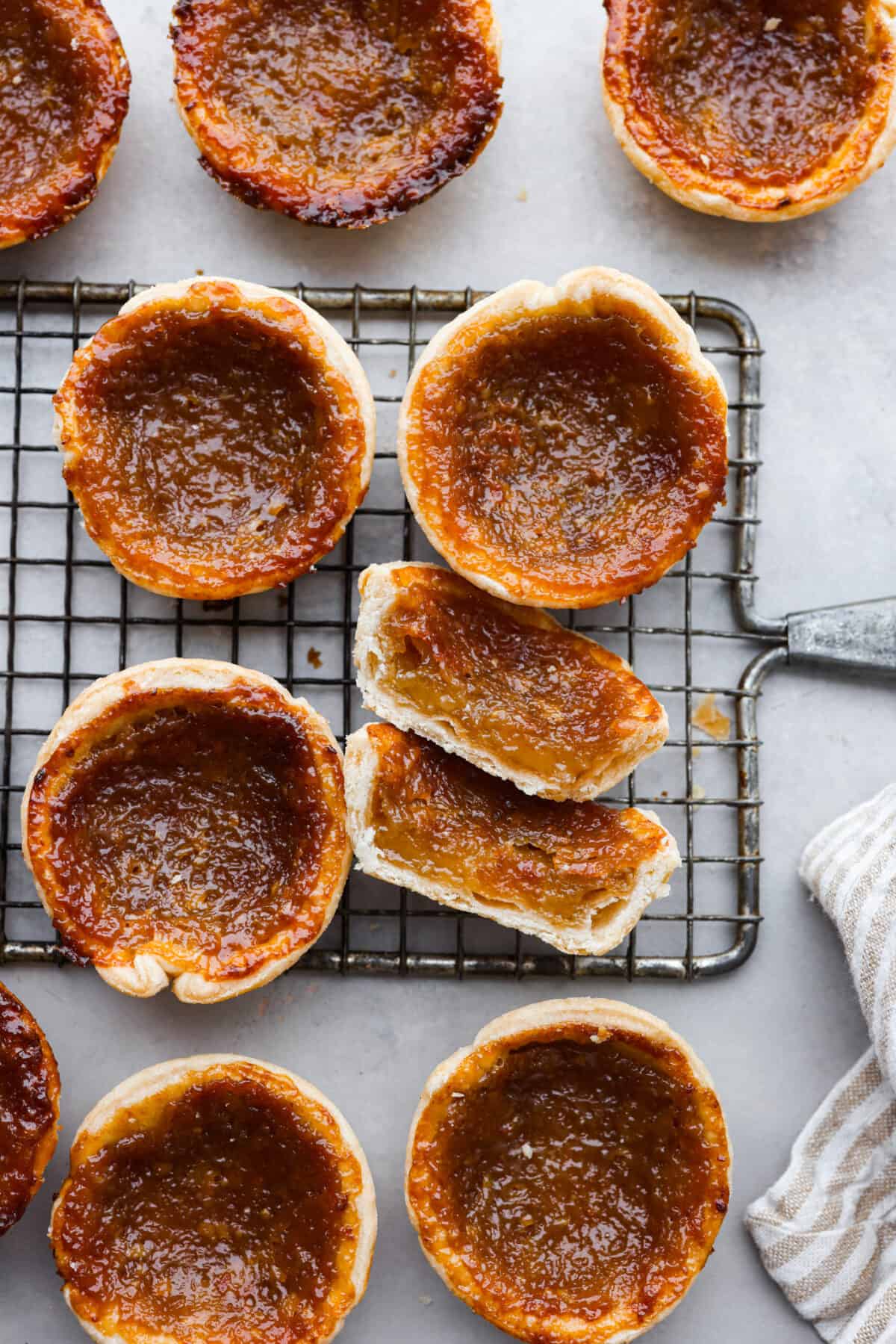 Rich and gooey Butter Tarts are the perfect treat for any occasion! They feature a sweet, buttery filling baked inside a flaky crust that will definitely make you want to keep going back for more!ย Top-down view of butter tarts on a wire rack. One is cut in half.
