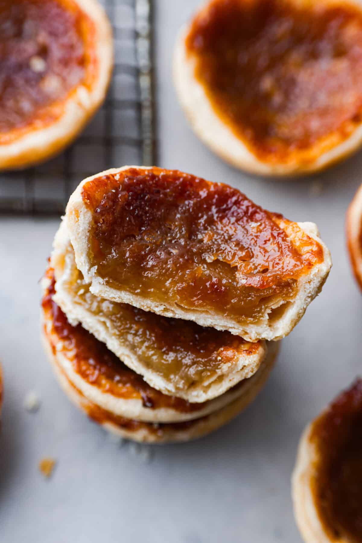 Rich and gooey Butter Tarts are the perfect treat for any occasion! They feature a sweet, buttery filling baked inside a flaky crust that will definitely make you want to keep going back for more!ย Closeup of butter tarts stacked on top of each other.