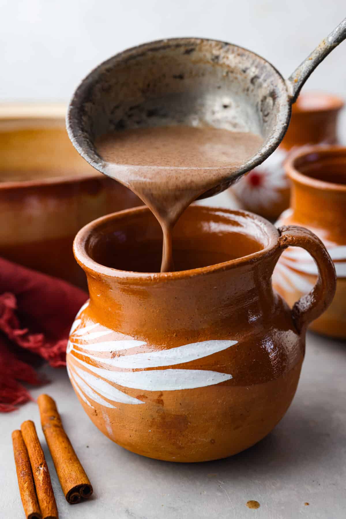 Get toasty from the inside out with champurrado, a delicious variation of Mexican hot chocolate! Deep, melty chocolate meets warming spices and brown sugar, all thickened with corn flour for a velvety smooth sip. Perfect for chasing any winter blues away! Pouring the beverage into a mug.