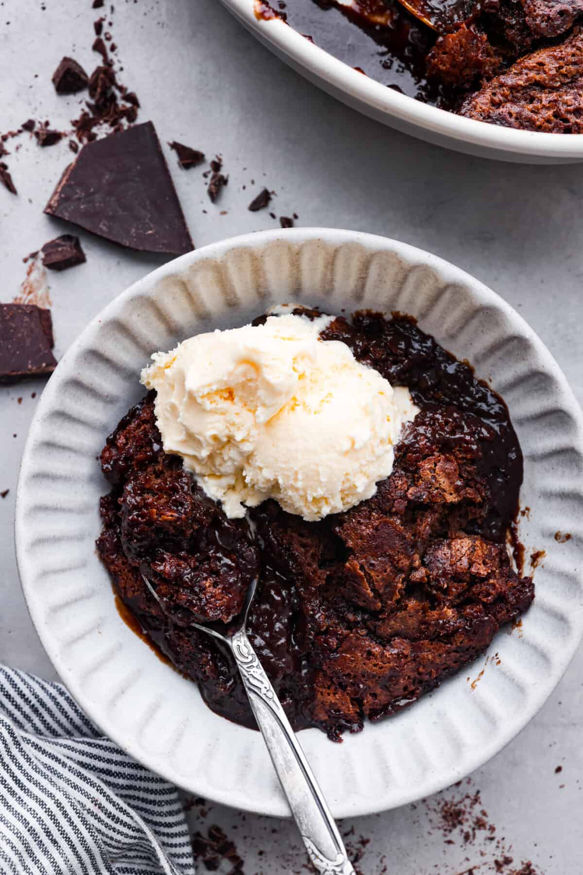 Everyone will want to eat dessert first with this Chocolate Cobbler โ a simple dessert that's all about gooey chocolate goodness. The velvety inside and crispy top create a perfect combo for a satisfying, easy-to-make treat! A bowl of chocolate cobbler with a silver spoon and a scoop of vanilla ice cream on top.