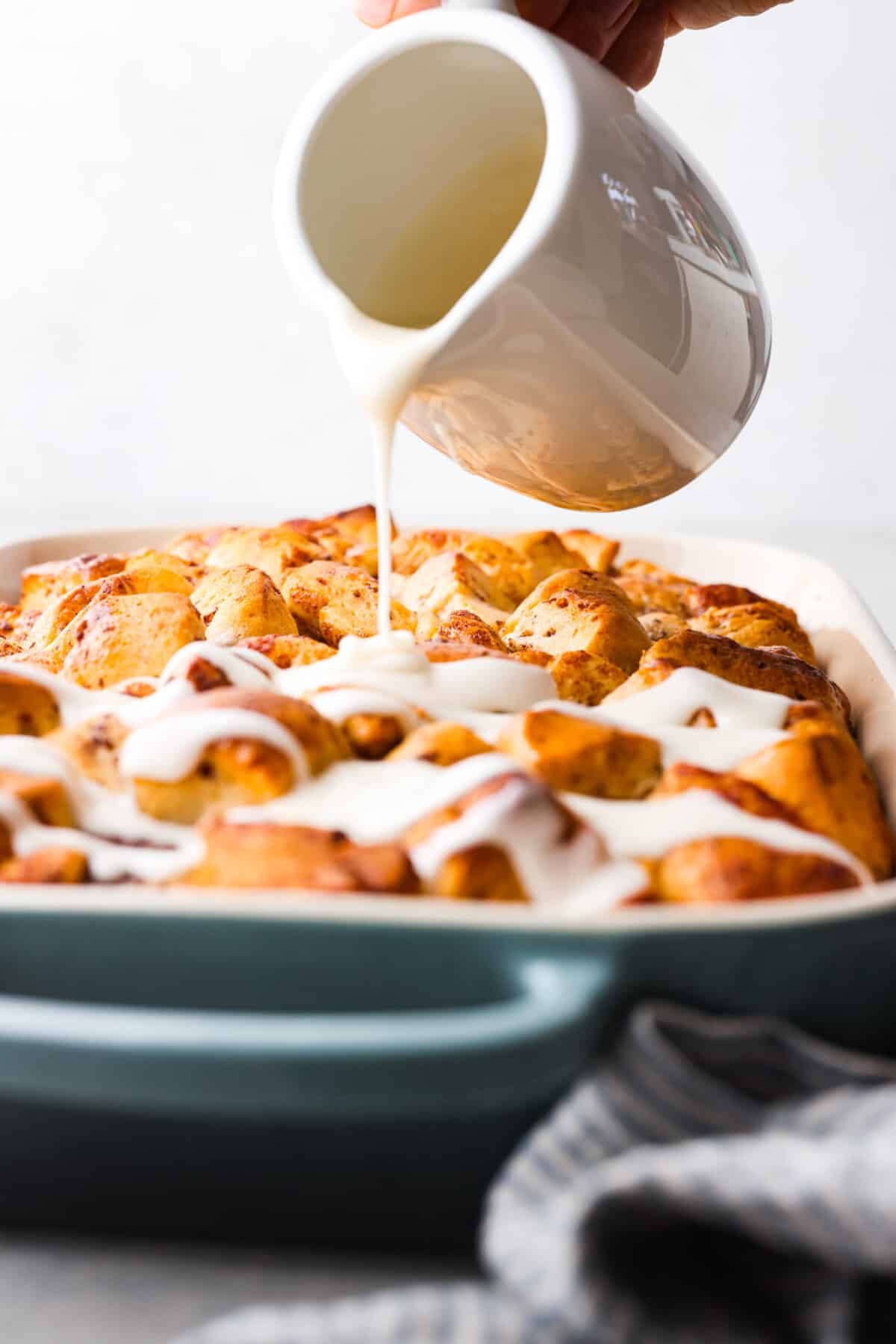 Get ready for a tasty treat with this easy cinnamon roll casserole! Using canned cinnamon rolls, this casserole is so delicious with creamy icing drizzled over warm, golden rolls. It's perfect for any breakfast or brunch! Icing being drizzled over baked cinnamon roll casserole.