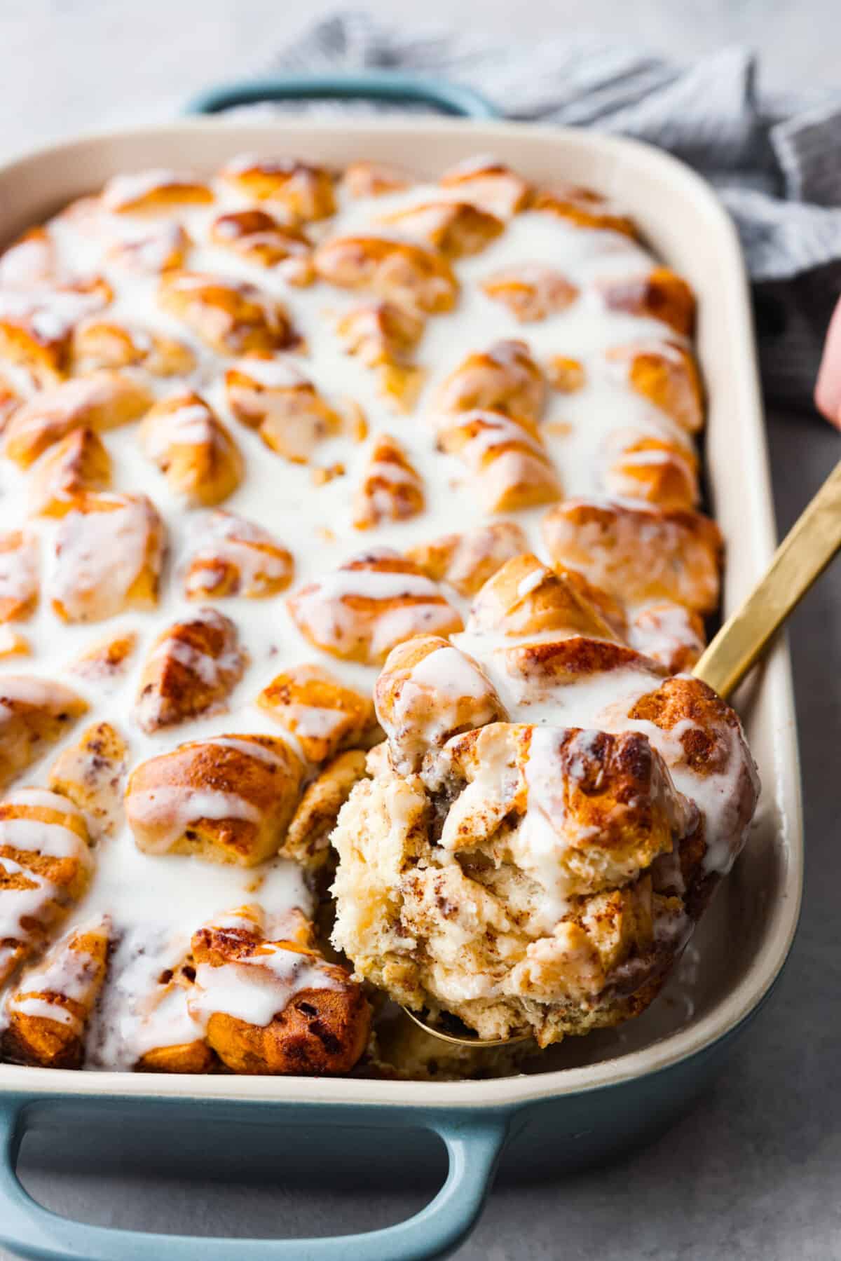 Get ready for a tasty treat with this easy cinnamon roll casserole! Using canned cinnamon rolls, this casserole is so delicious with creamy icing drizzled over warm, golden rolls. It's perfect for any breakfast or brunch! A casserole dish with cinnamon roll casserole baked and ready to eat. One slice being dished out with a gold spoon.