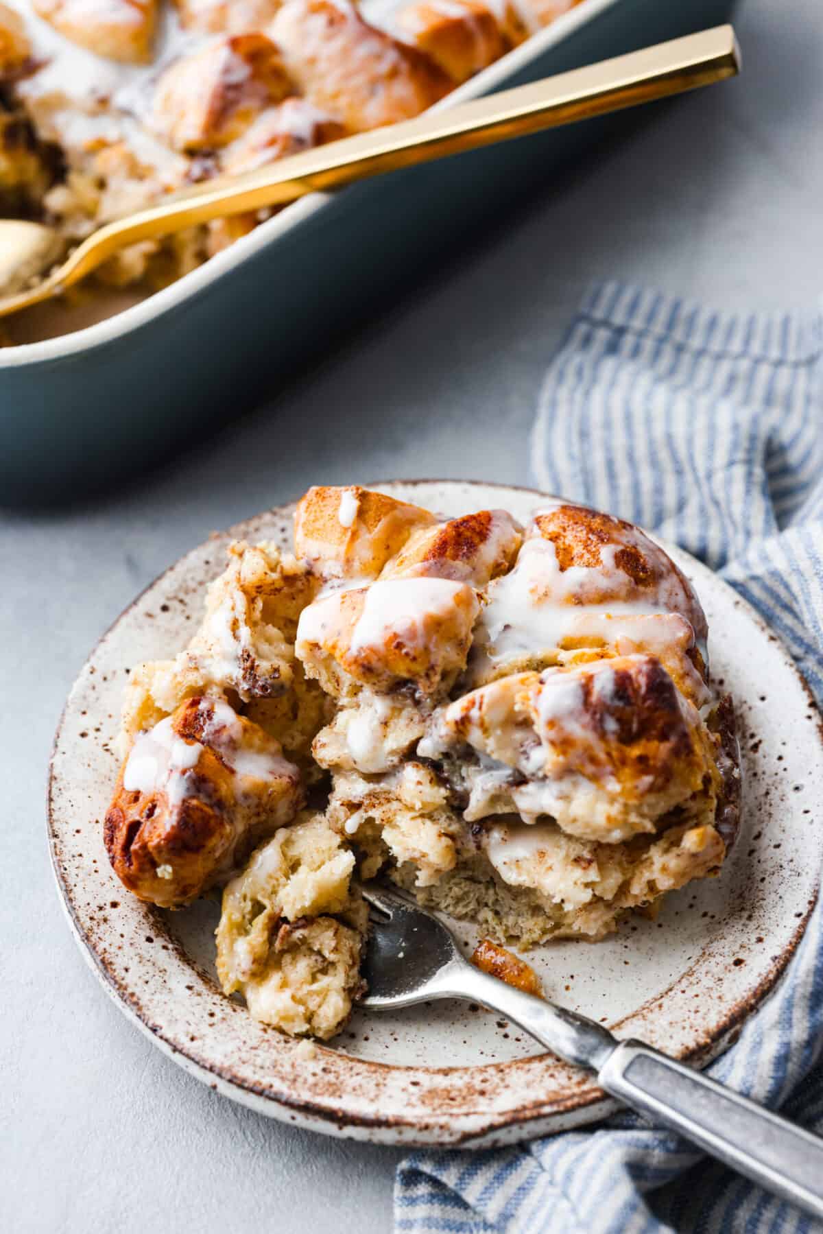 Get ready for a tasty treat with this easy cinnamon roll casserole! Using canned cinnamon rolls, this casserole is so delicious with creamy icing drizzled over warm, golden rolls. It's perfect for any breakfast or brunch! Cinnamon roll casserole on a plate with a fork.