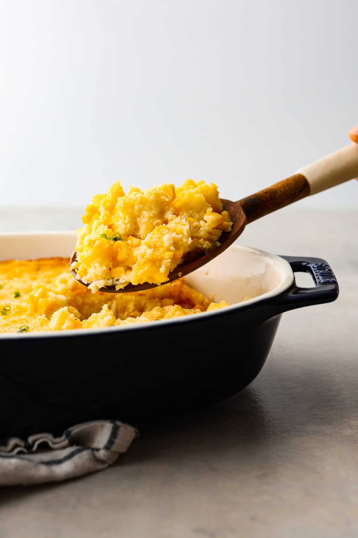 5 Ingredient Corn Casserole is in the oven for less than five minutes. It's the perfect side dish for the holidays with almost no effort at all! A scoop of corn casserole being taken out of the dish with a wooden spoon.