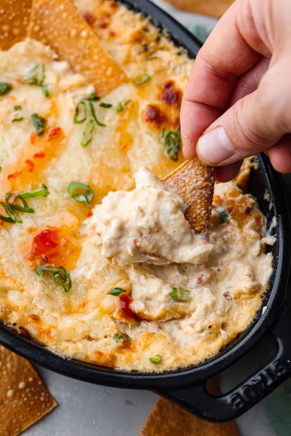 We are obsessed with this crab rangoon dip! It’s hot, creamy, cheesy and packed with crab and major flavor. It's sure to become your go-to appetizer when you really want to impress! Closeup of a fried wonton chip being dipped into the hot crab dip.