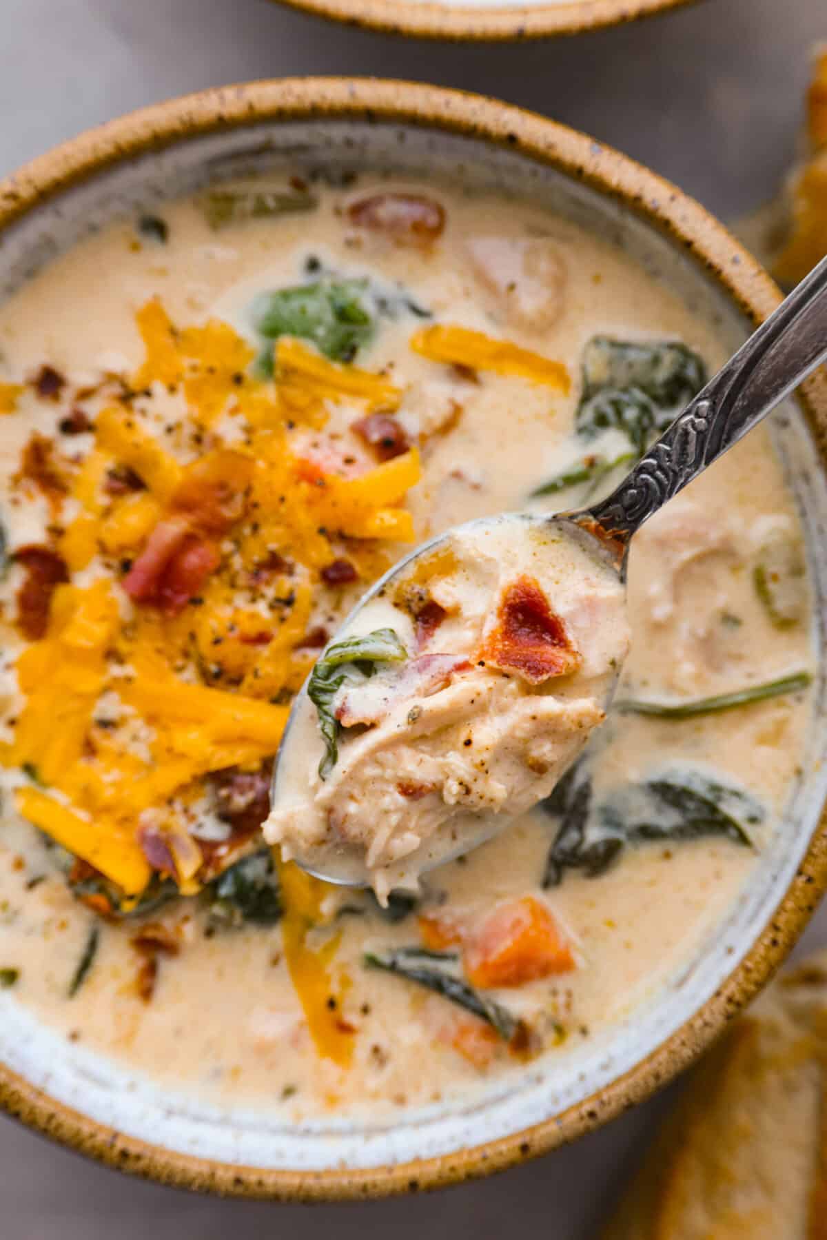 All it takes is one bite to obsess over this crack chicken soup! It's loaded with shredded chicken, bacon, ranch seasonings, and all of your favorite creamy crack-inspired flavors! Top view of a spoon lifting soup out of a bowl.