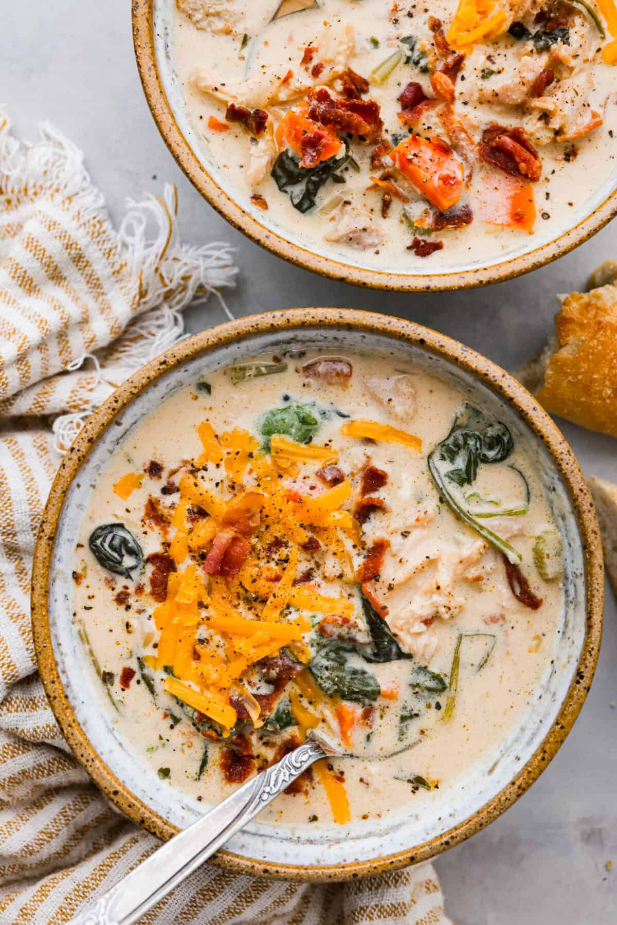All it takes is one bite to obsess over this crack chicken soup! It's loaded with shredded chicken, bacon, ranch seasonings, and all of your favorite creamy crack-inspired flavors! Top view of crack chicken soup in two bowls with shredded cheese on top.