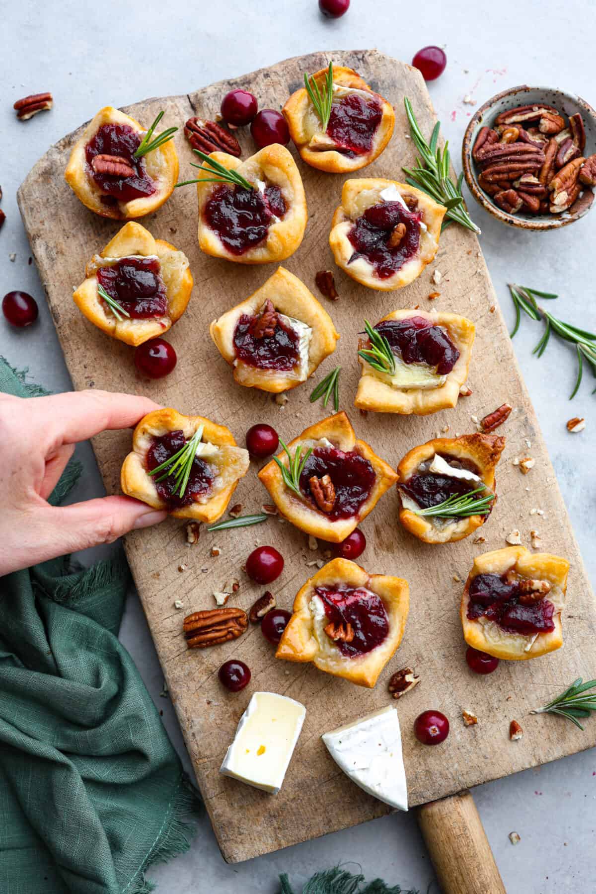 Cranberry pecan brie bites are such an amazing appetizer! It has layered pecans, soft brie, and a dollop of cranberry sauce, all cupped in a golden brown, flaky crescent roll!ย The top view of cranberry brie bites on a wooden platter.